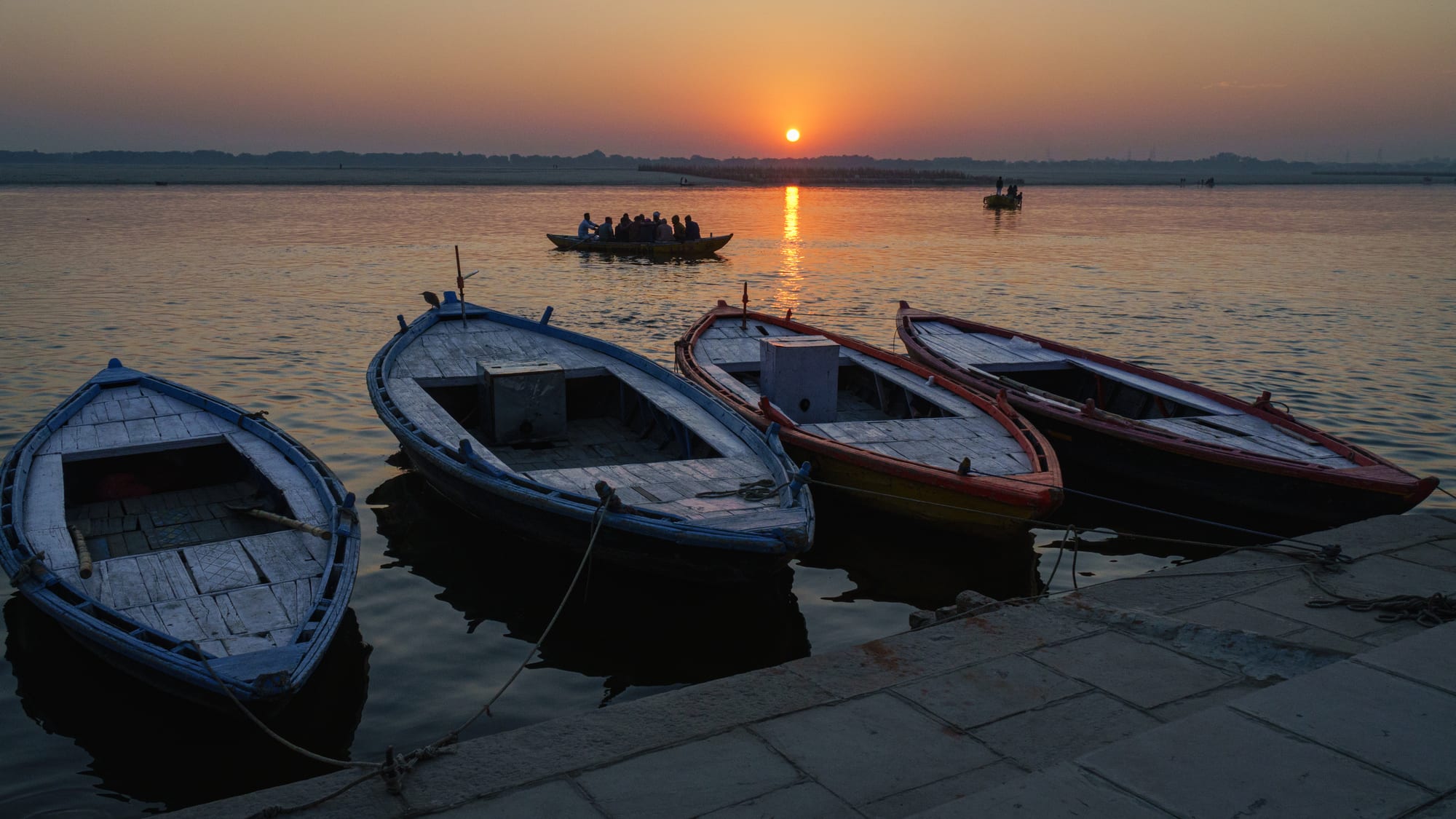 Wooden rowing boats moored at stone steps on a wide calm river as the sun rises over the far bank