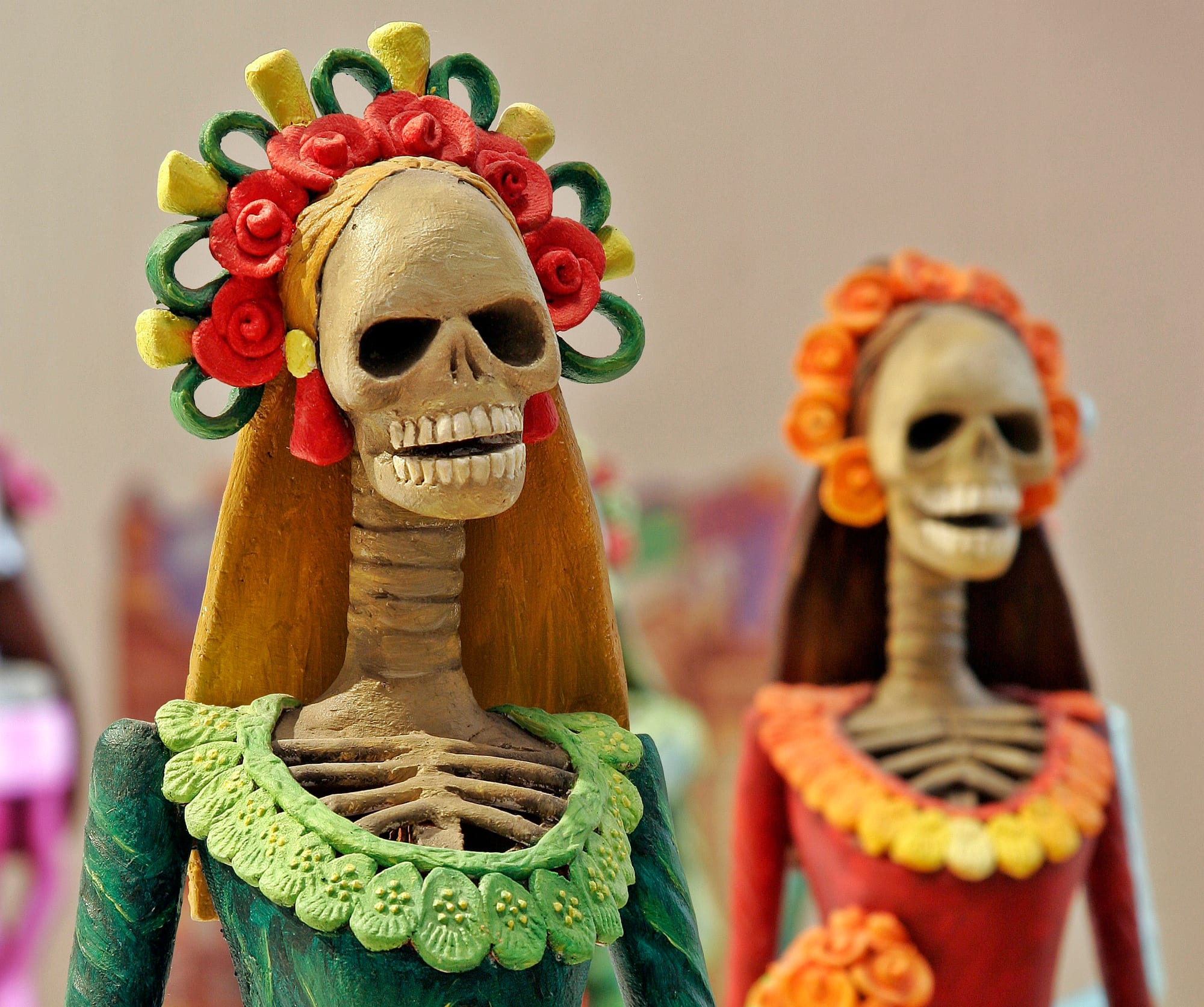 Two painted skeleton figures of women, one wearing a green dress and a crown of red roses, the other in red with orange flowers
