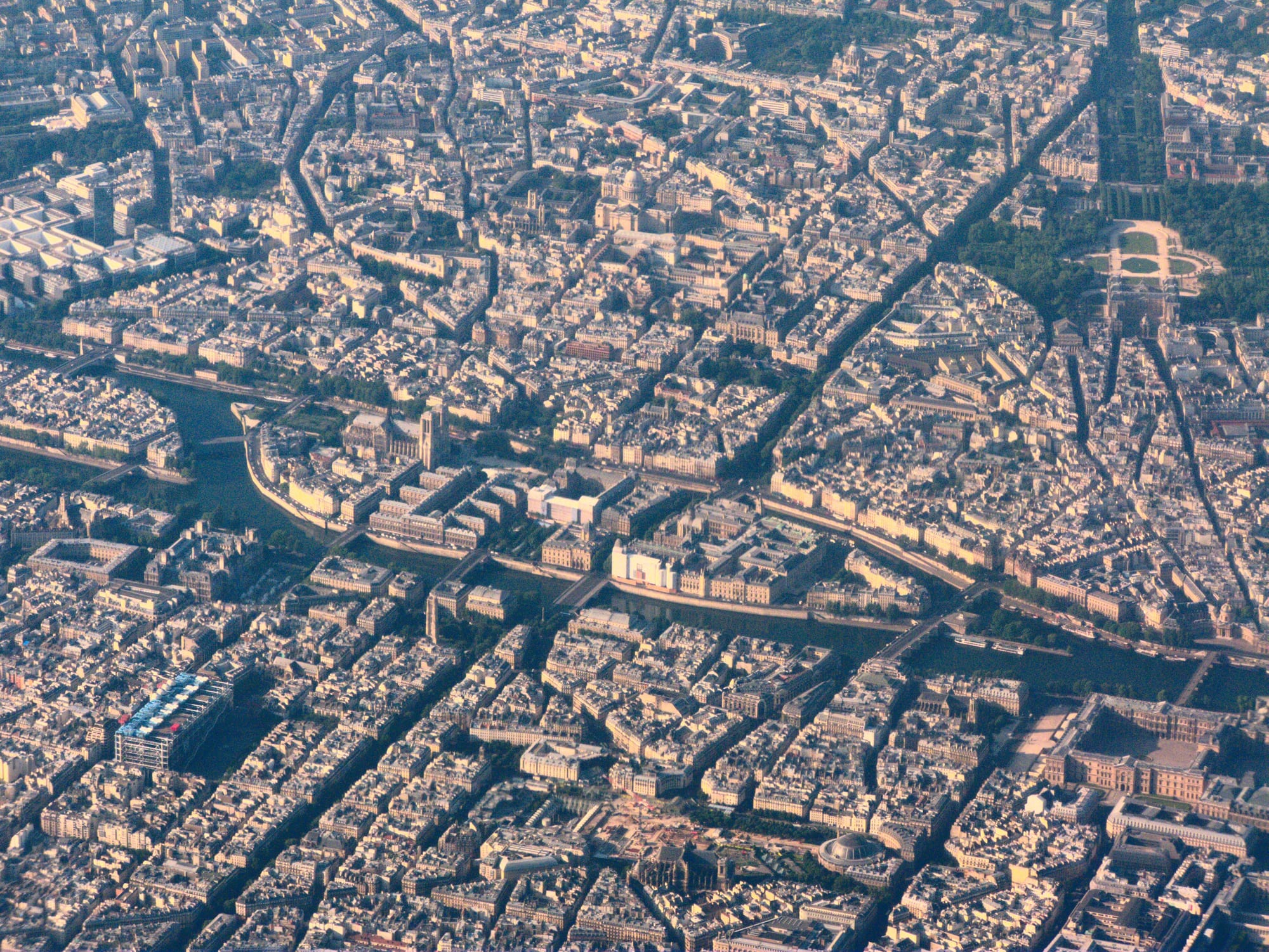 An aerial view of a dense city of pale stone buildings with an island in a curving river at its centre