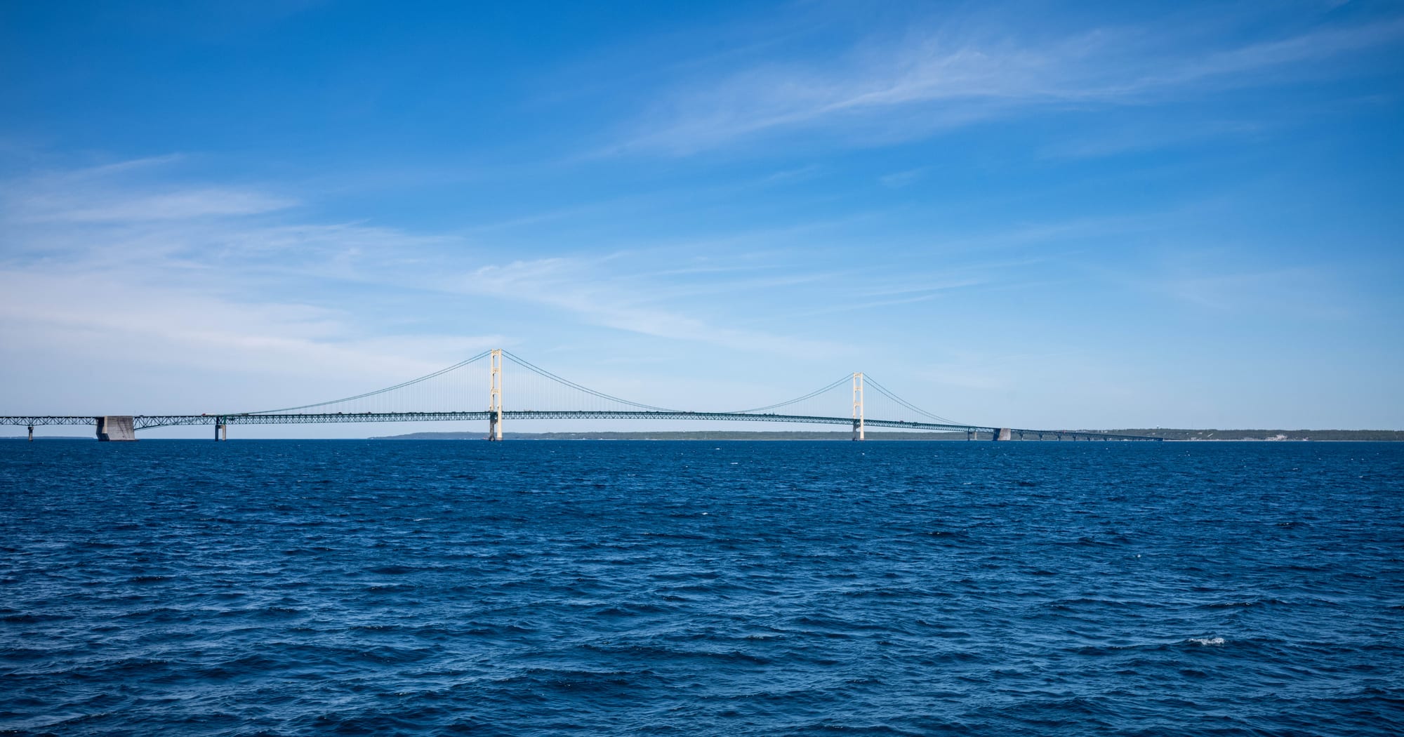 A long suspension bridge with two tall towers stretching across deep blue water under a clear sky