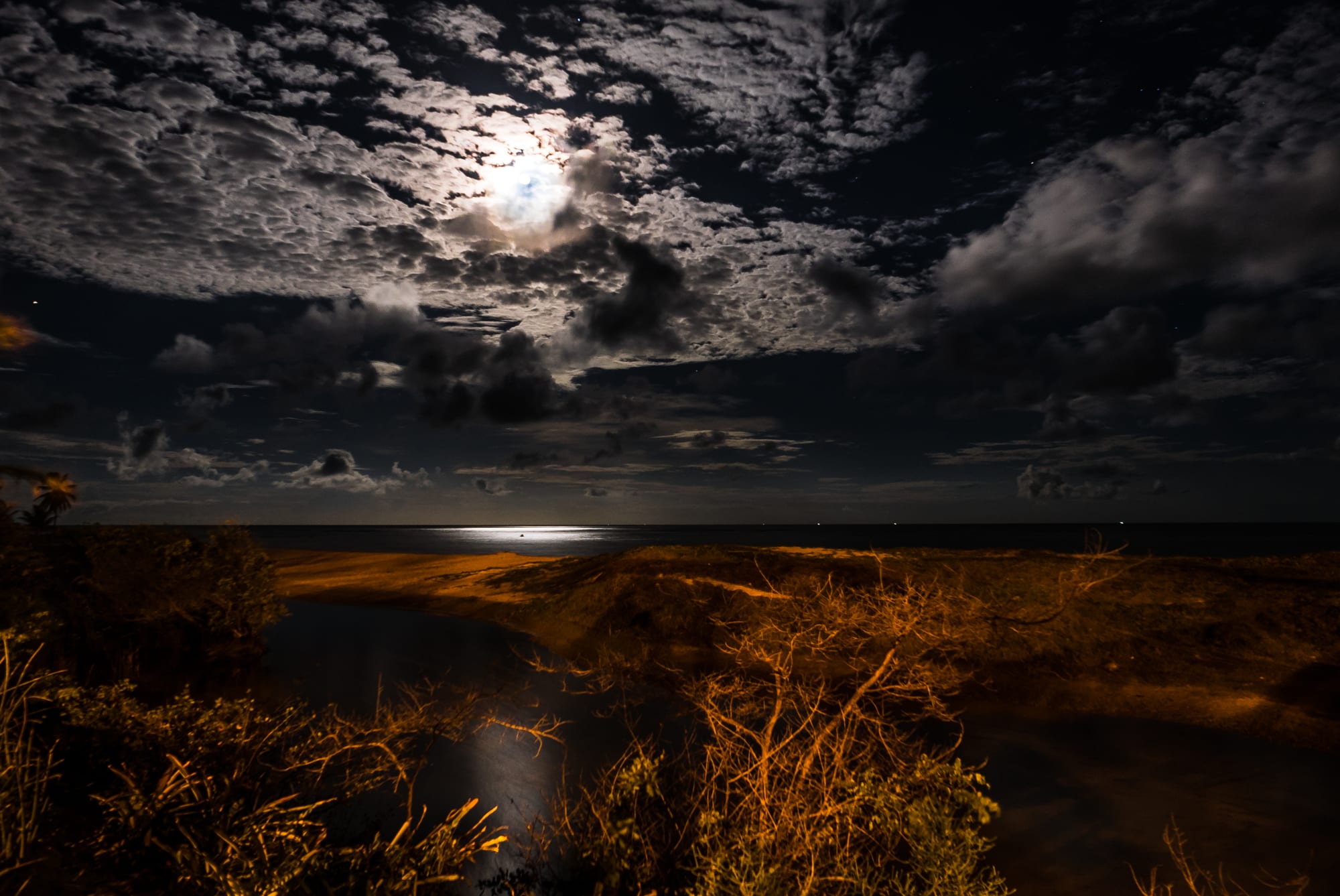 A bright full moon shining through broken clouds above a dark sea