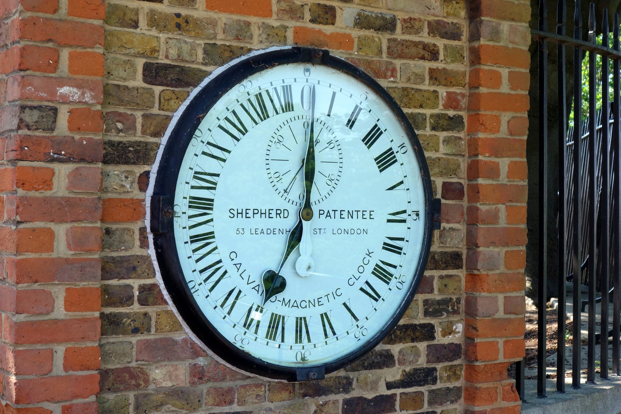 A large round clock face with a 24-hour dial of Roman numerals mounted on a brick wall