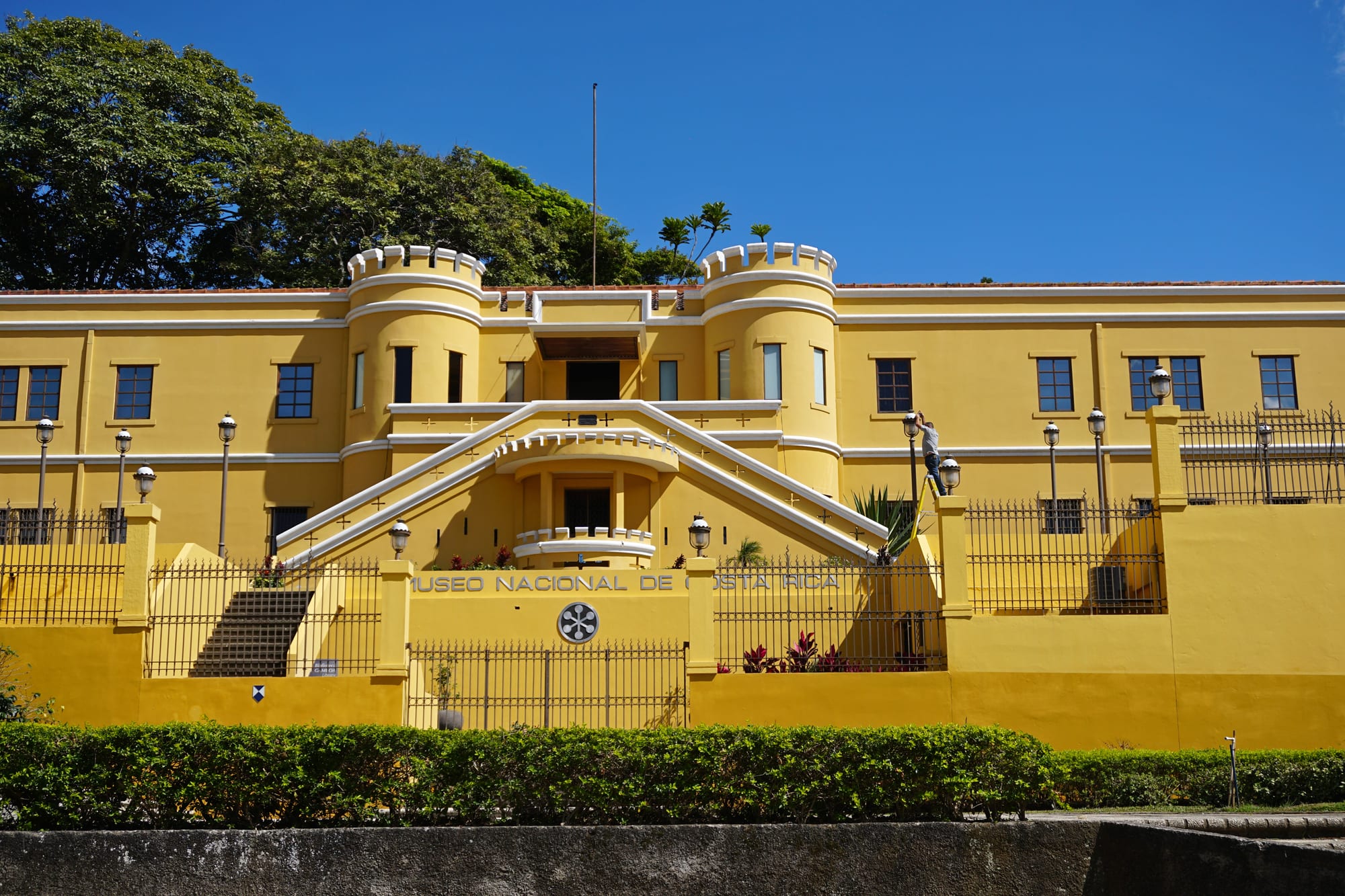 A long yellow fortress-like building with two crenellated round towers, a double staircase and a sign reading Museo Nacional de Costa Rica