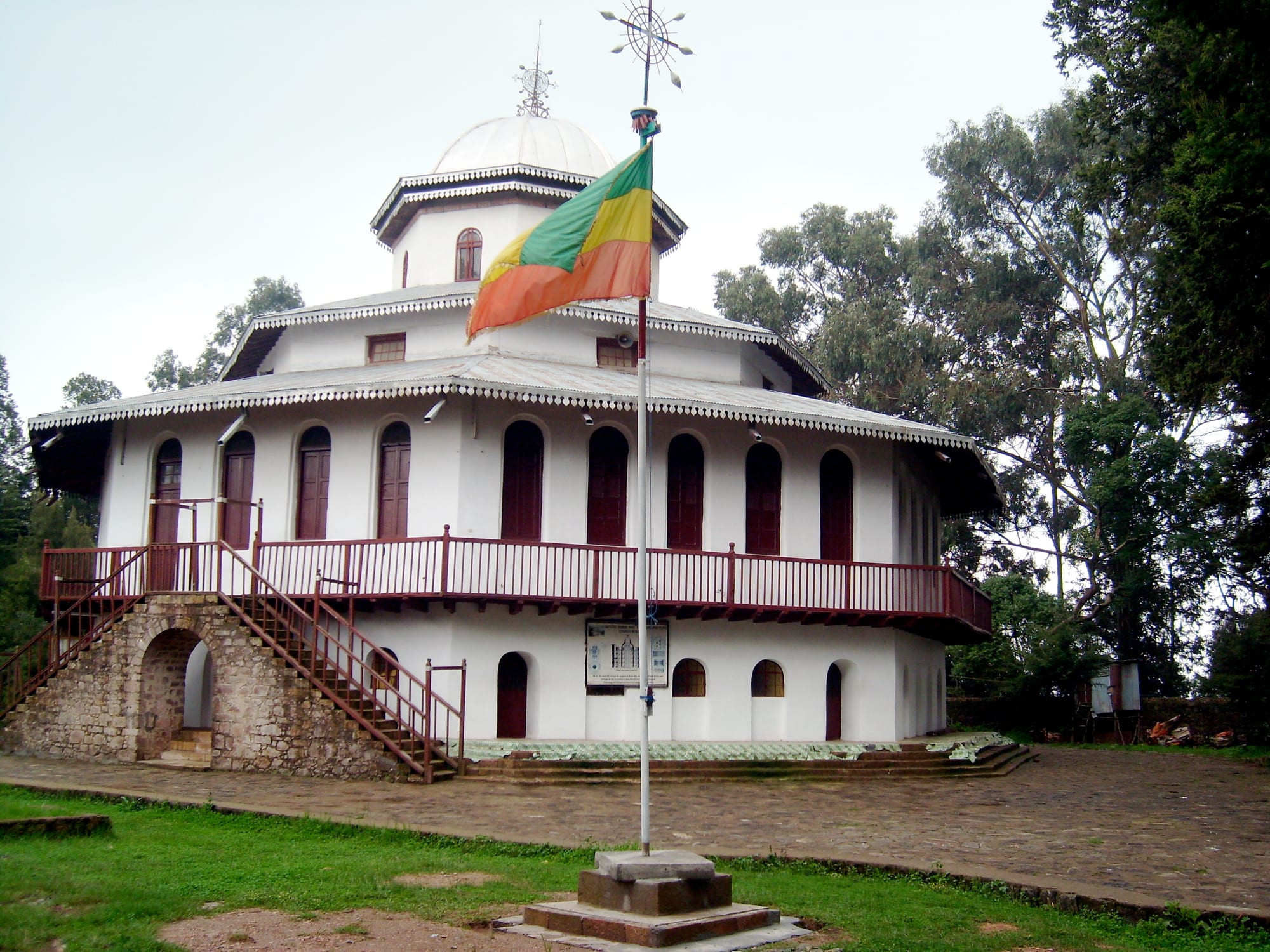 A white octagonal church with a domed roof, arched windows and a red-railed balcony, with the Ethiopian flag flying in front