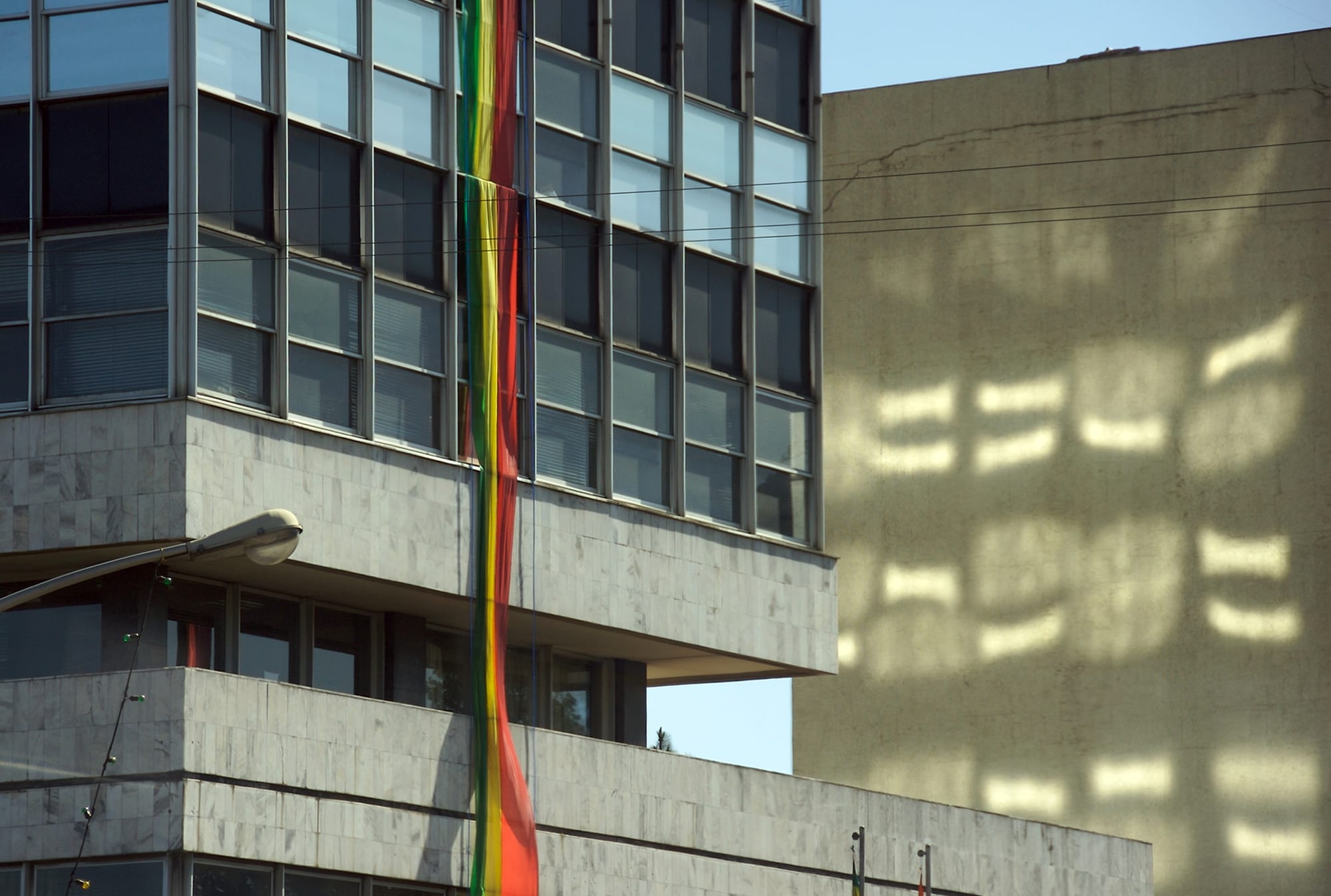 A long ribbon of green, yellow and red bunting hanging down the glass and marble front of an office building