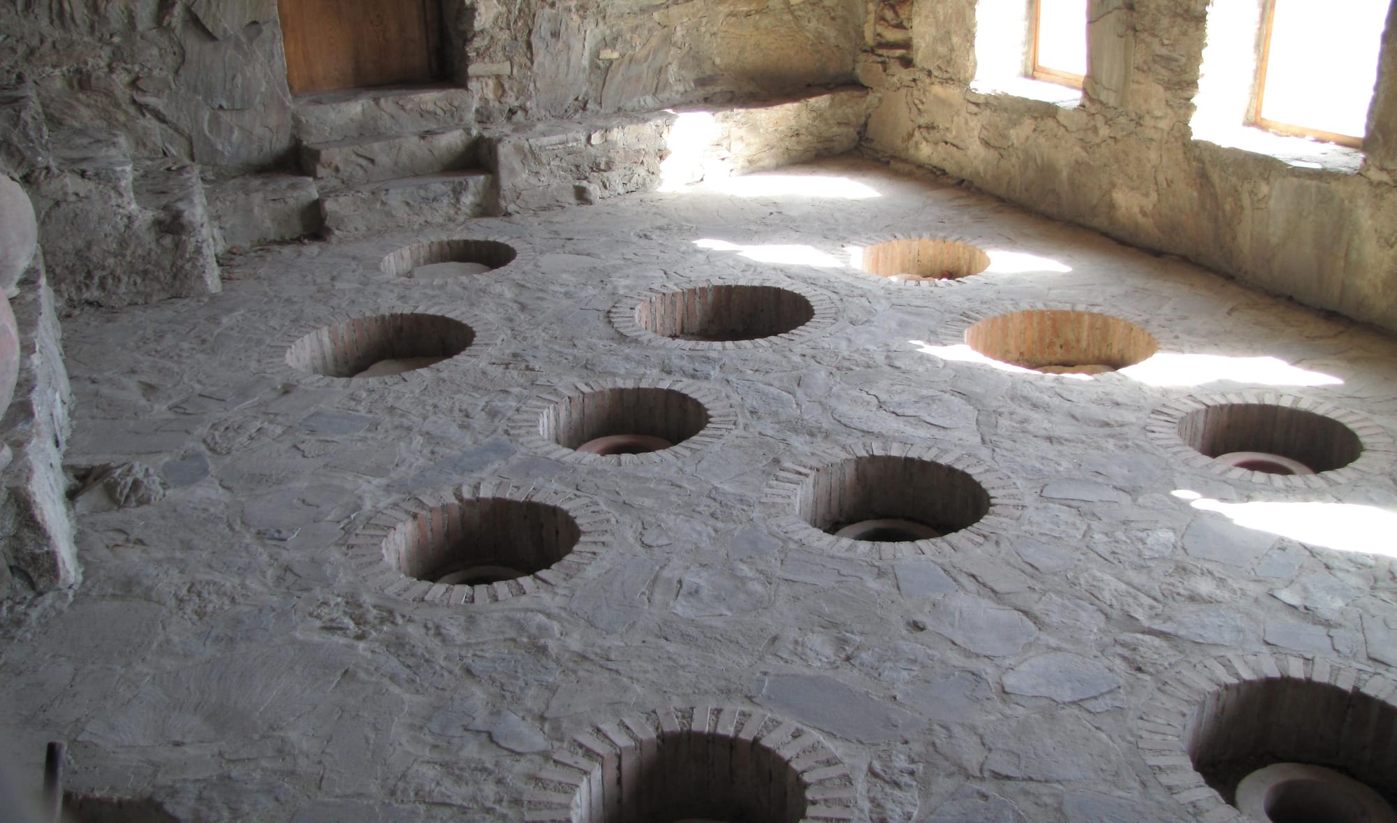 Sunlight falling on a stone floor set with rows of round brick-rimmed openings in an old cellar
