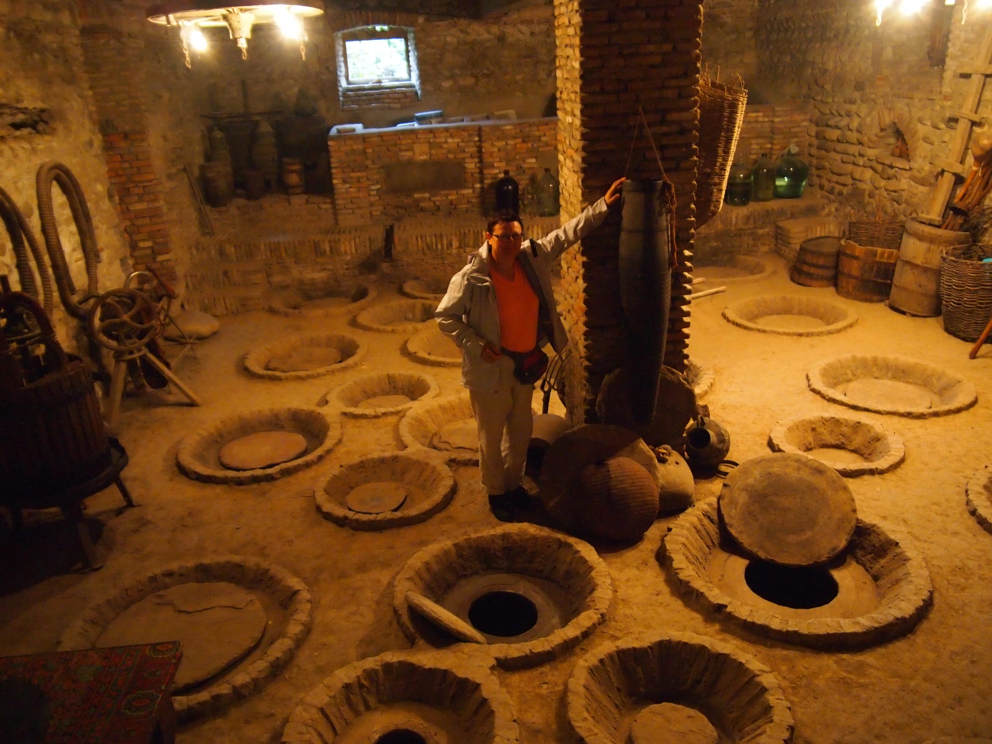 A dim stone cellar floor with rows of round openings, some covered with clay lids, marking clay jars buried in the ground