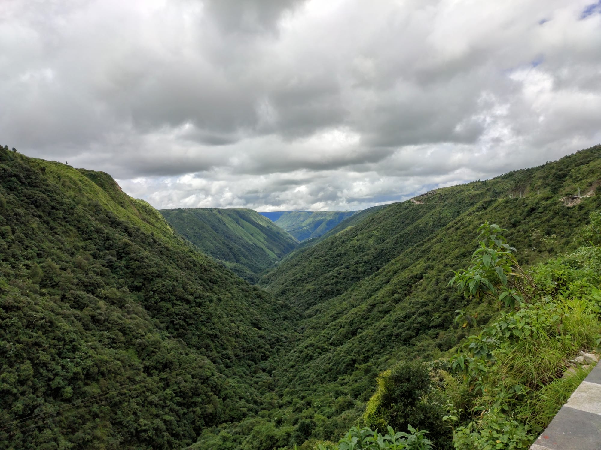 A deep, steep-sided green valley winding away under a sky of heavy grey cloud