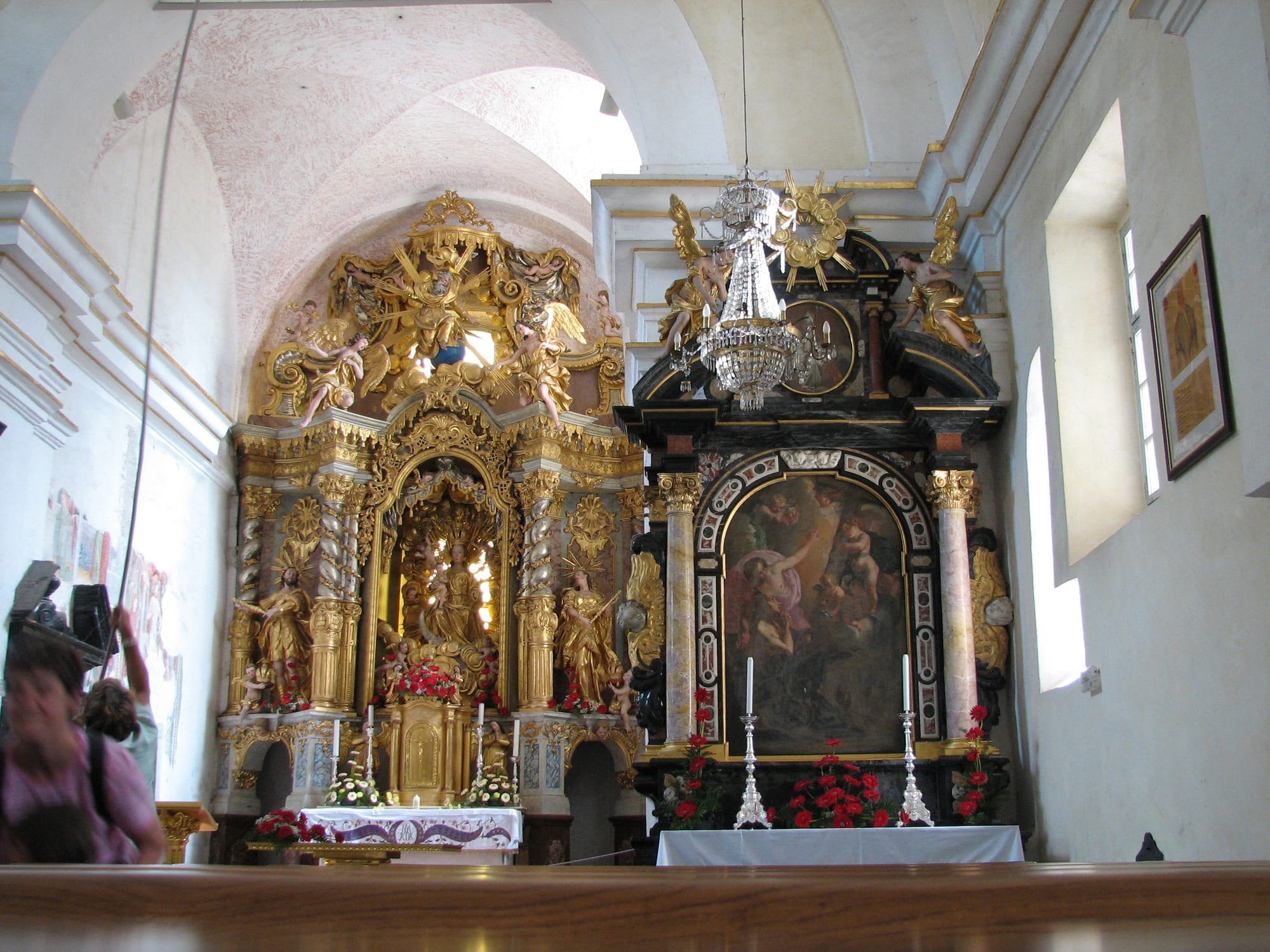 A church interior with a gilded carved altar full of statues and angels, and a black and coloured marble side altar with a painting