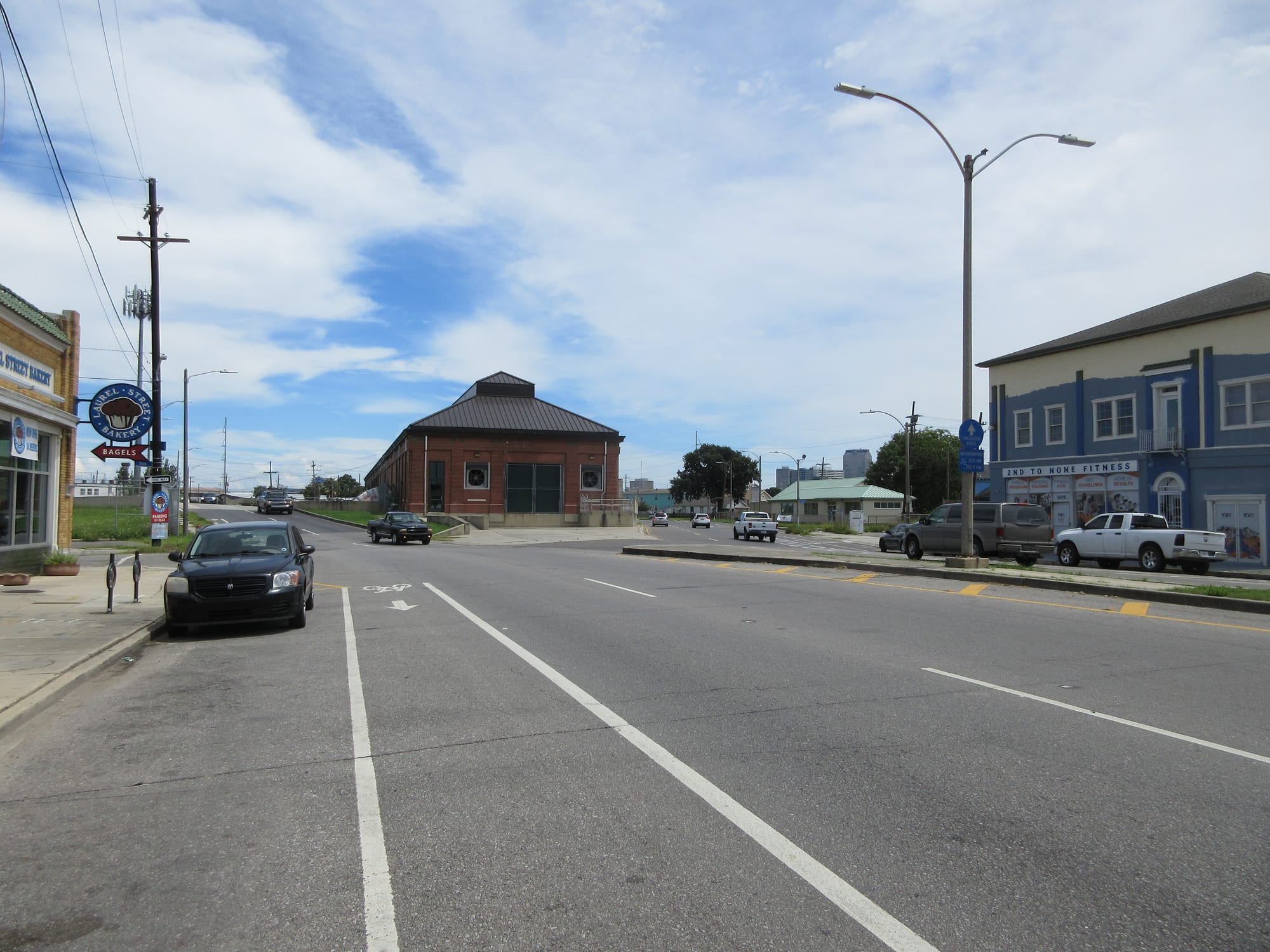 A red-brick industrial building with a hipped roof at the end of a wide street lined with shops