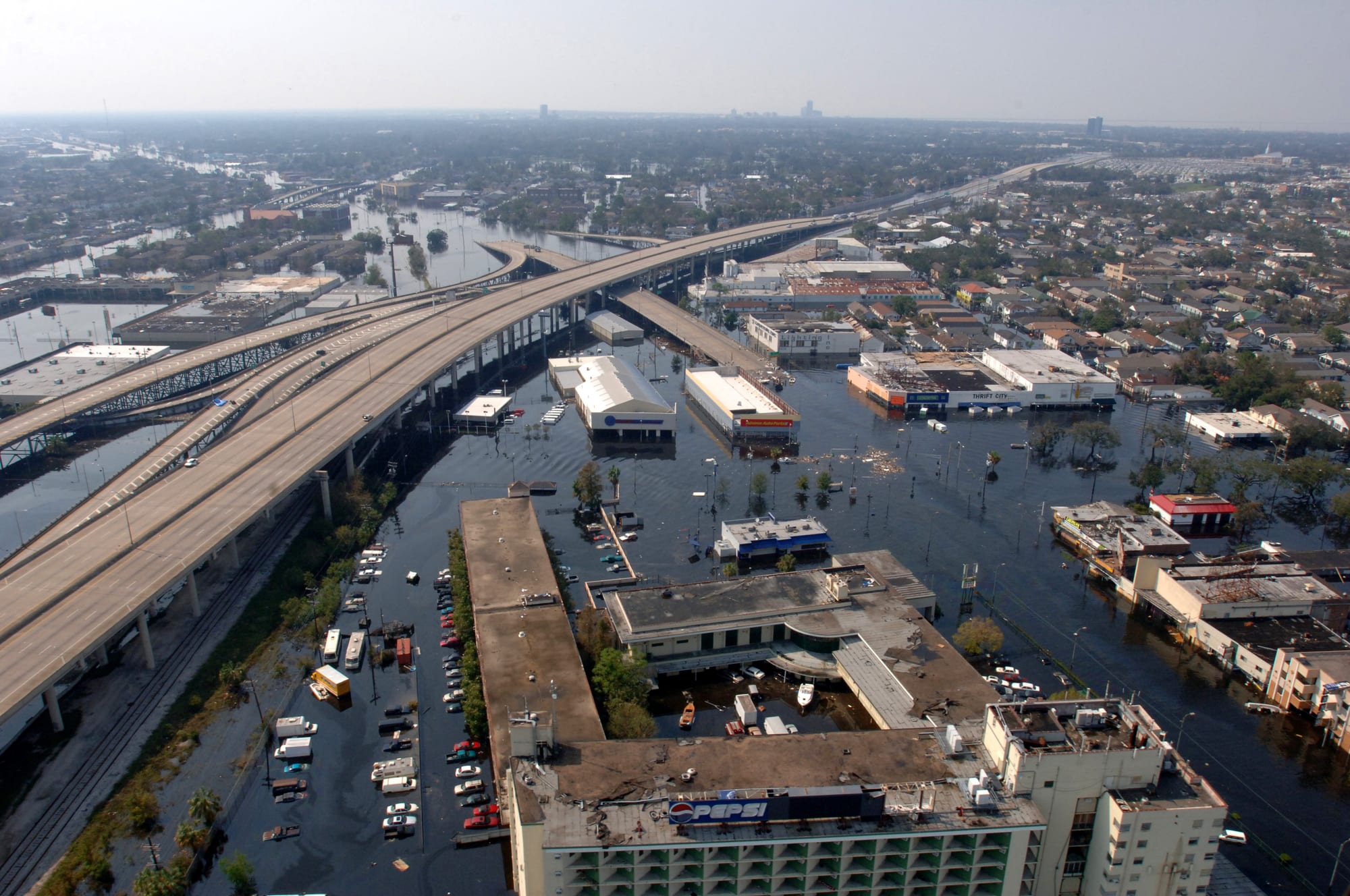 An aerial view of city streets, parking lots and low buildings standing in brown floodwater beside raised highways