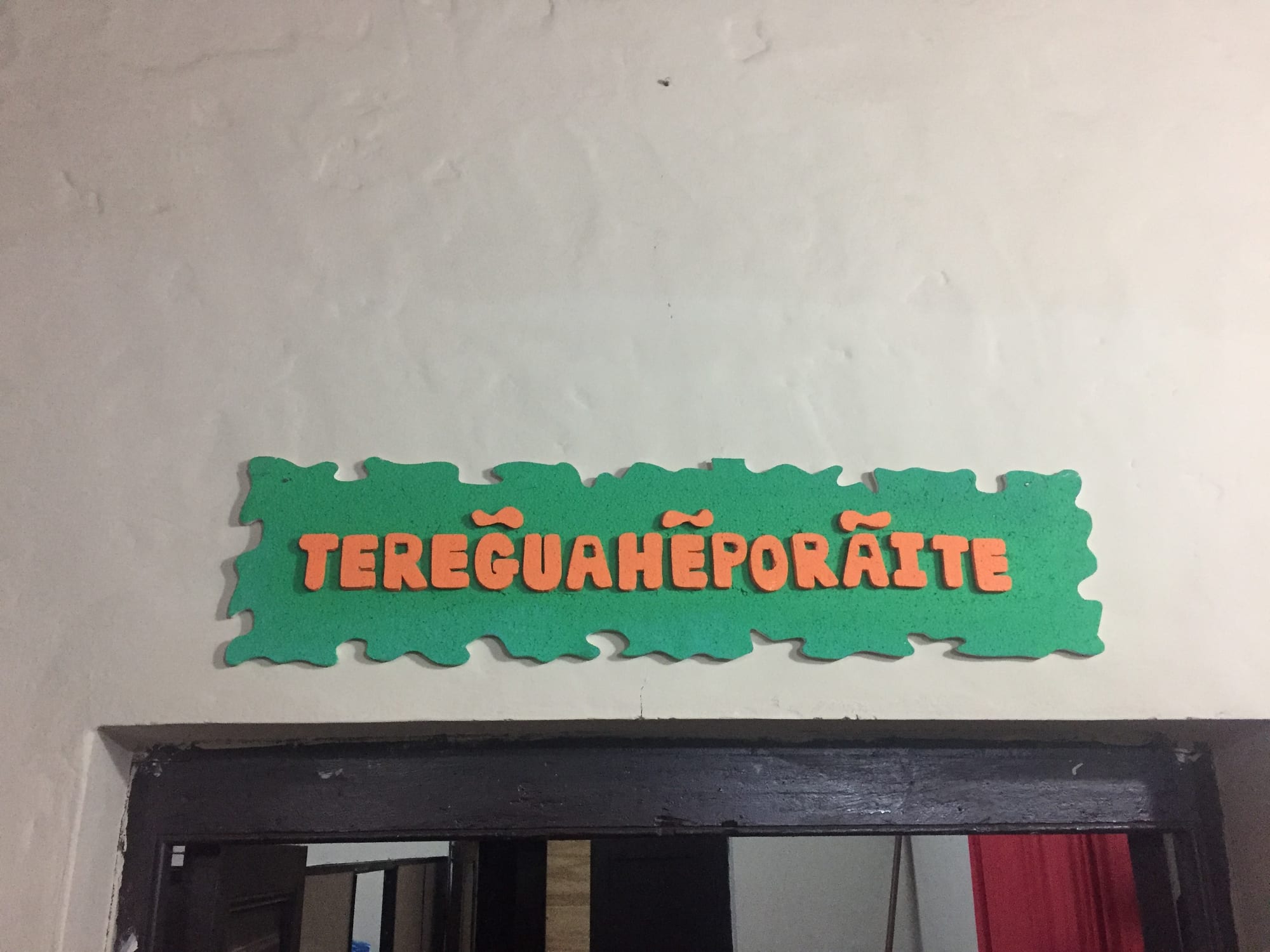 A green sign with orange letters reading TEREGUAHẼPORÃITE above a doorway on a white wall