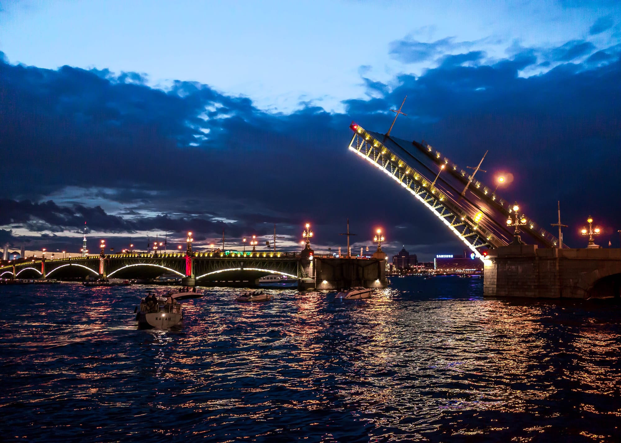 One span of a lit-up bridge raised high above a dark river under a blue night sky with clouds