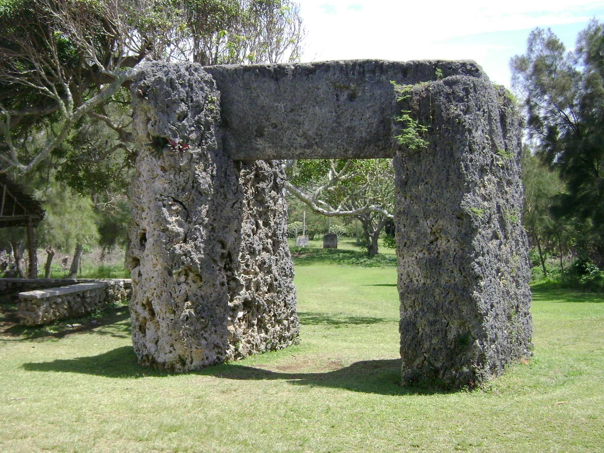 A huge gateway of two upright weathered coral-stone slabs topped by a stone lintel on a grassy lawn