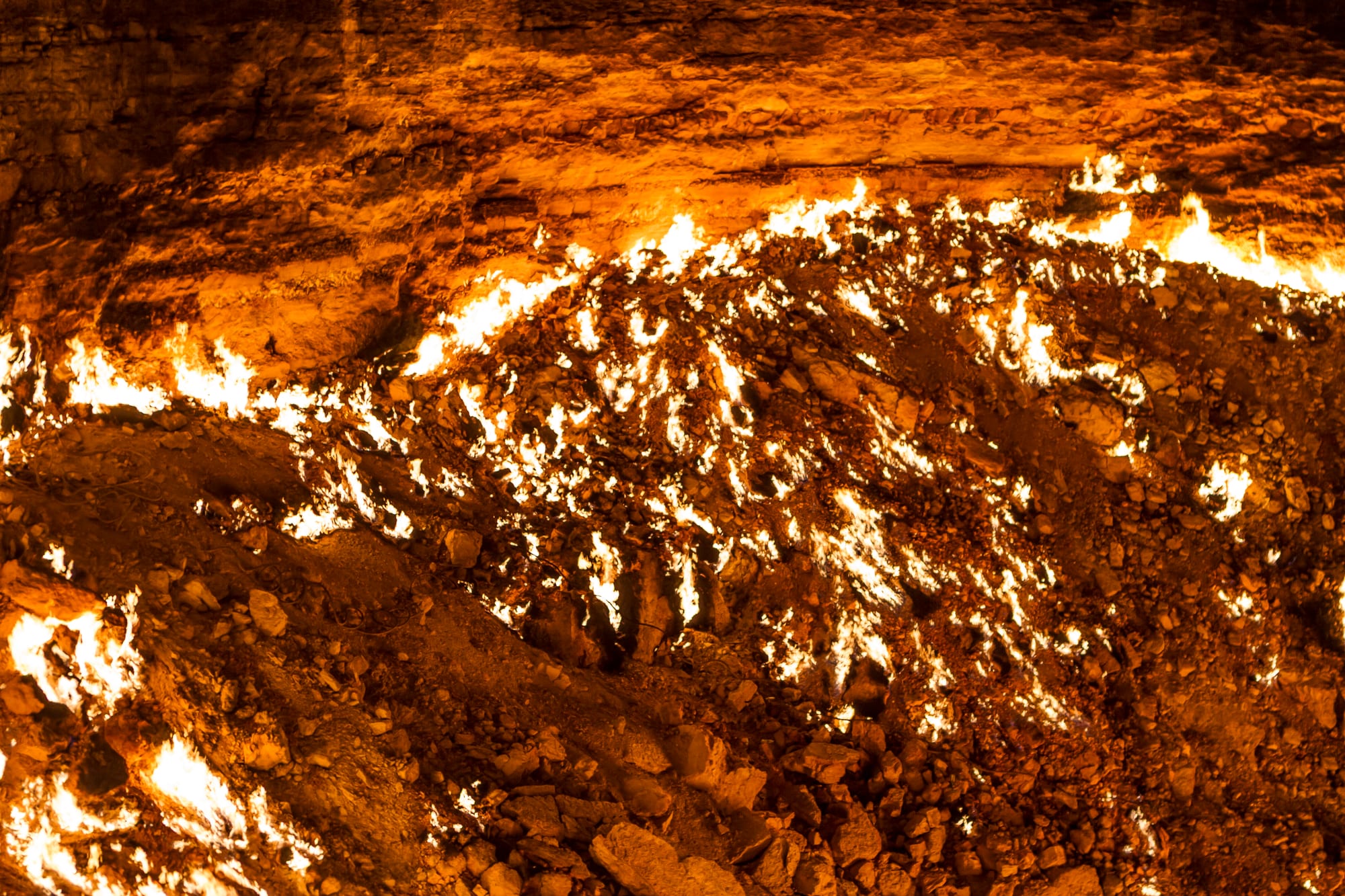 Close view of a rocky slope inside a pit, covered in hundreds of small white and orange flames