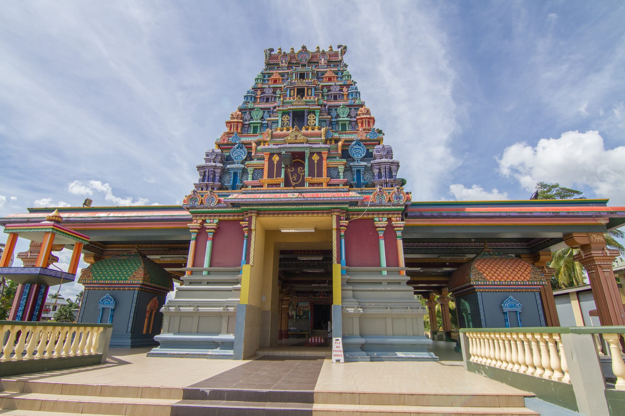 A tall Hindu temple tower covered in brightly painted carved figures, under a blue sky