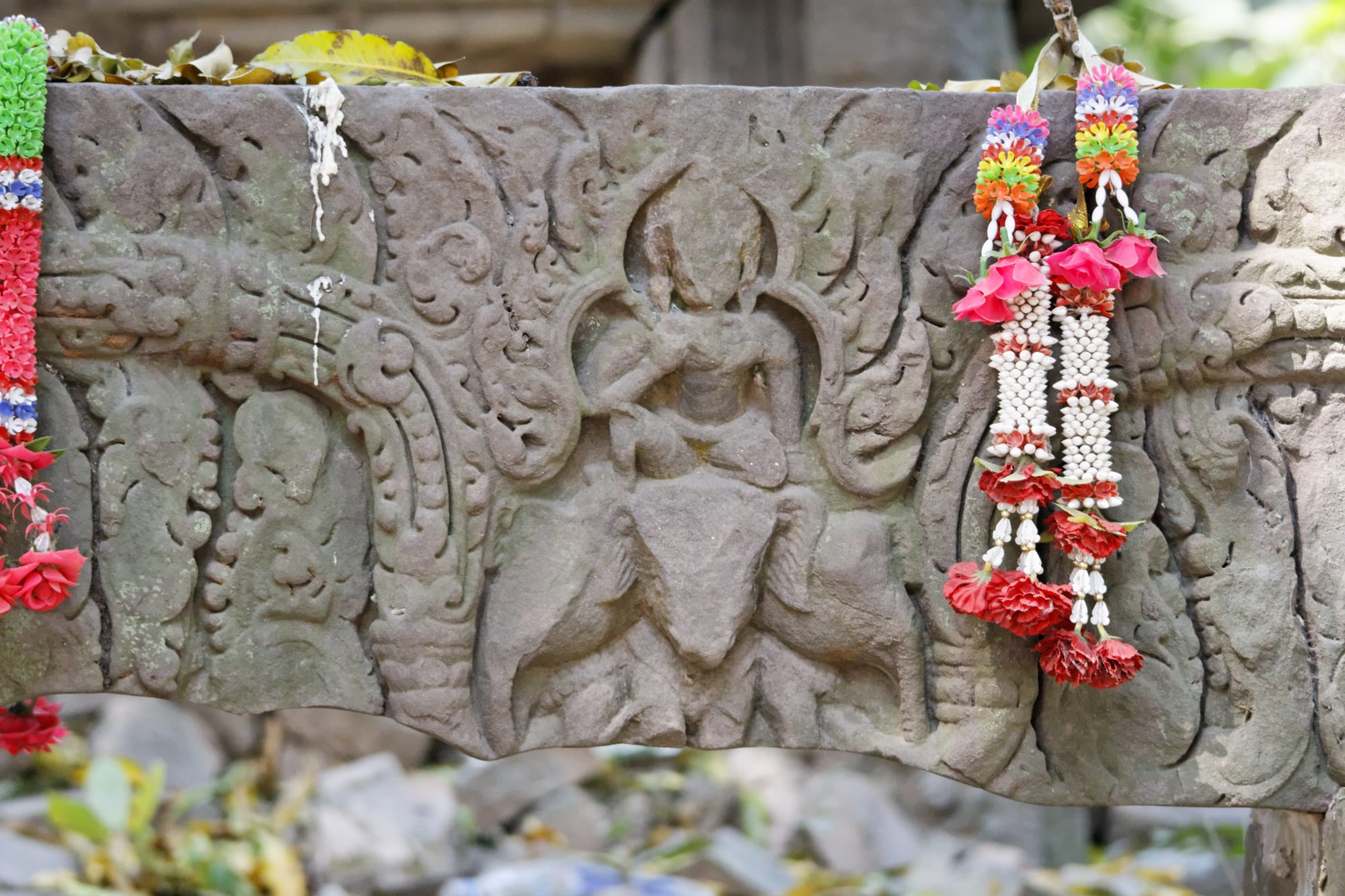 A weathered sandstone lintel carved with a figure seated on an elephant, hung with garlands of flowers