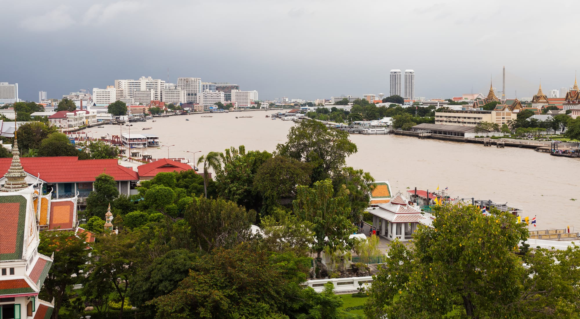 A broad brown river curving through a city of low buildings and trees, with temple spires on the far bank