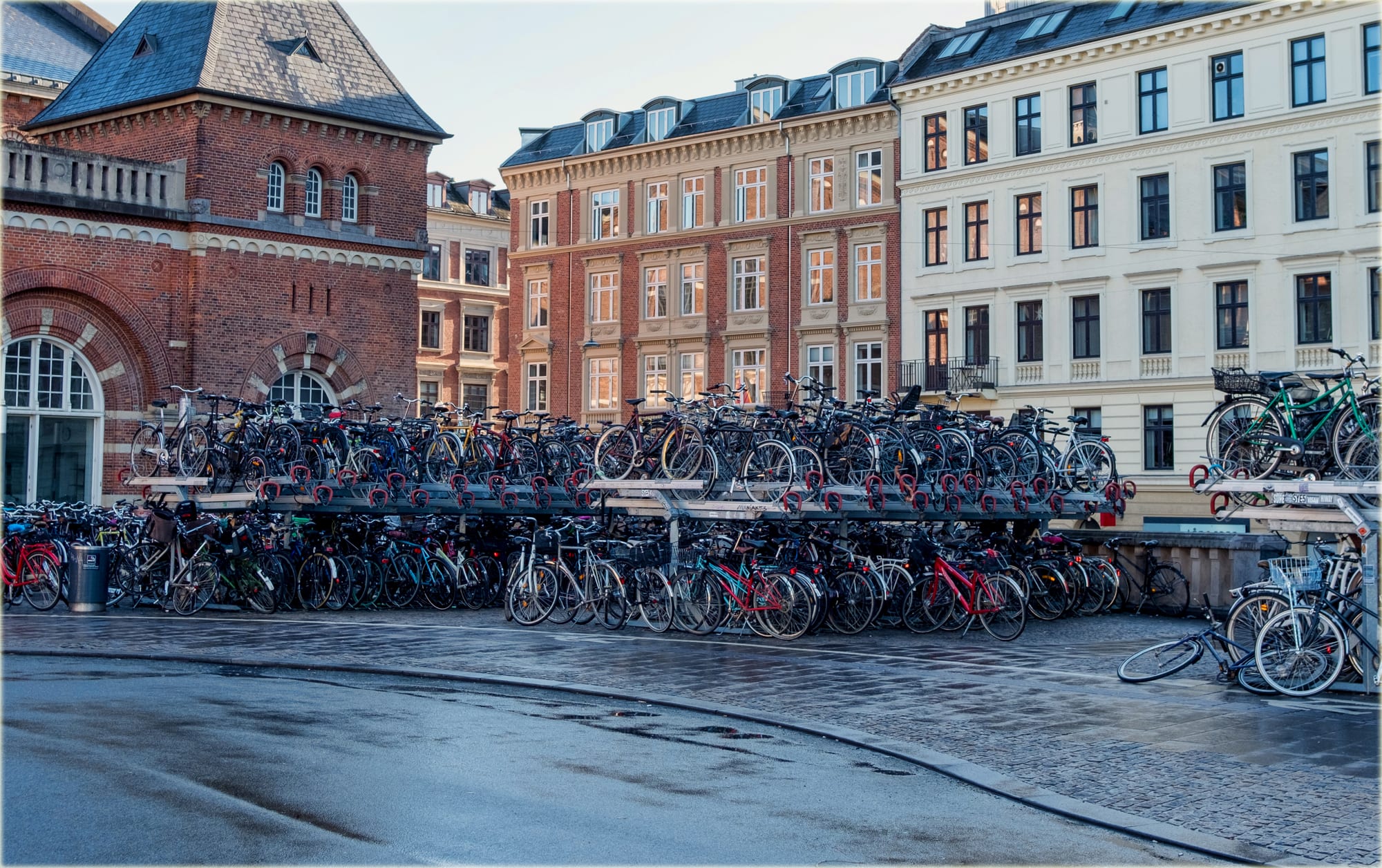 Hundreds of bicycles packed into two-tier racks in front of red-brick and cream apartment buildings on a wet street