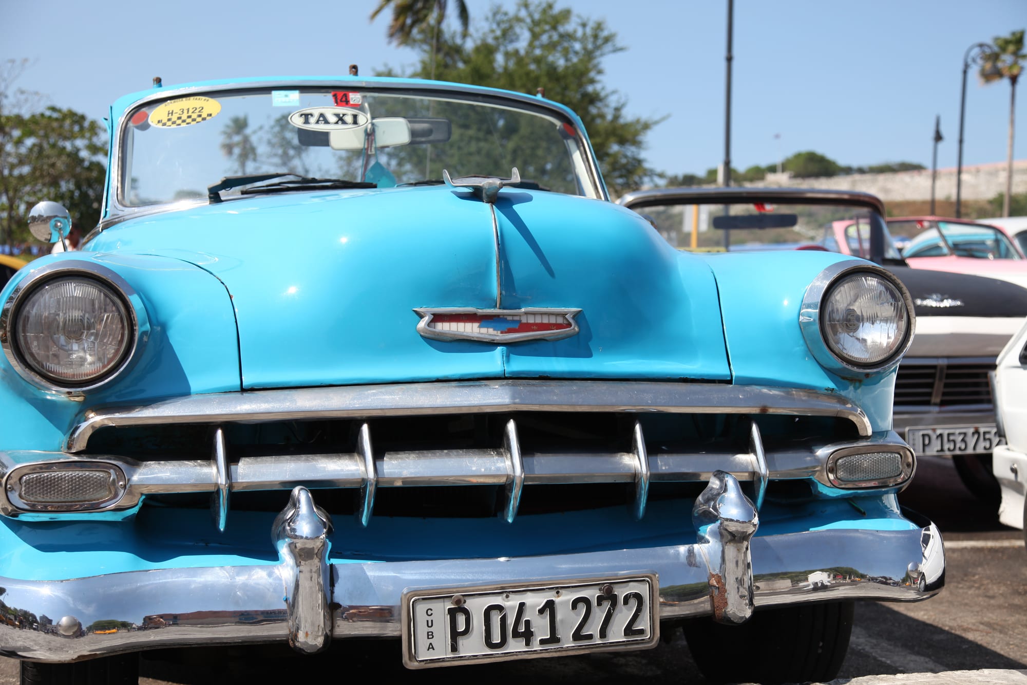 The bright blue front of a 1950s Chevrolet with a chrome grille, round headlights and a taxi sign in the windscreen