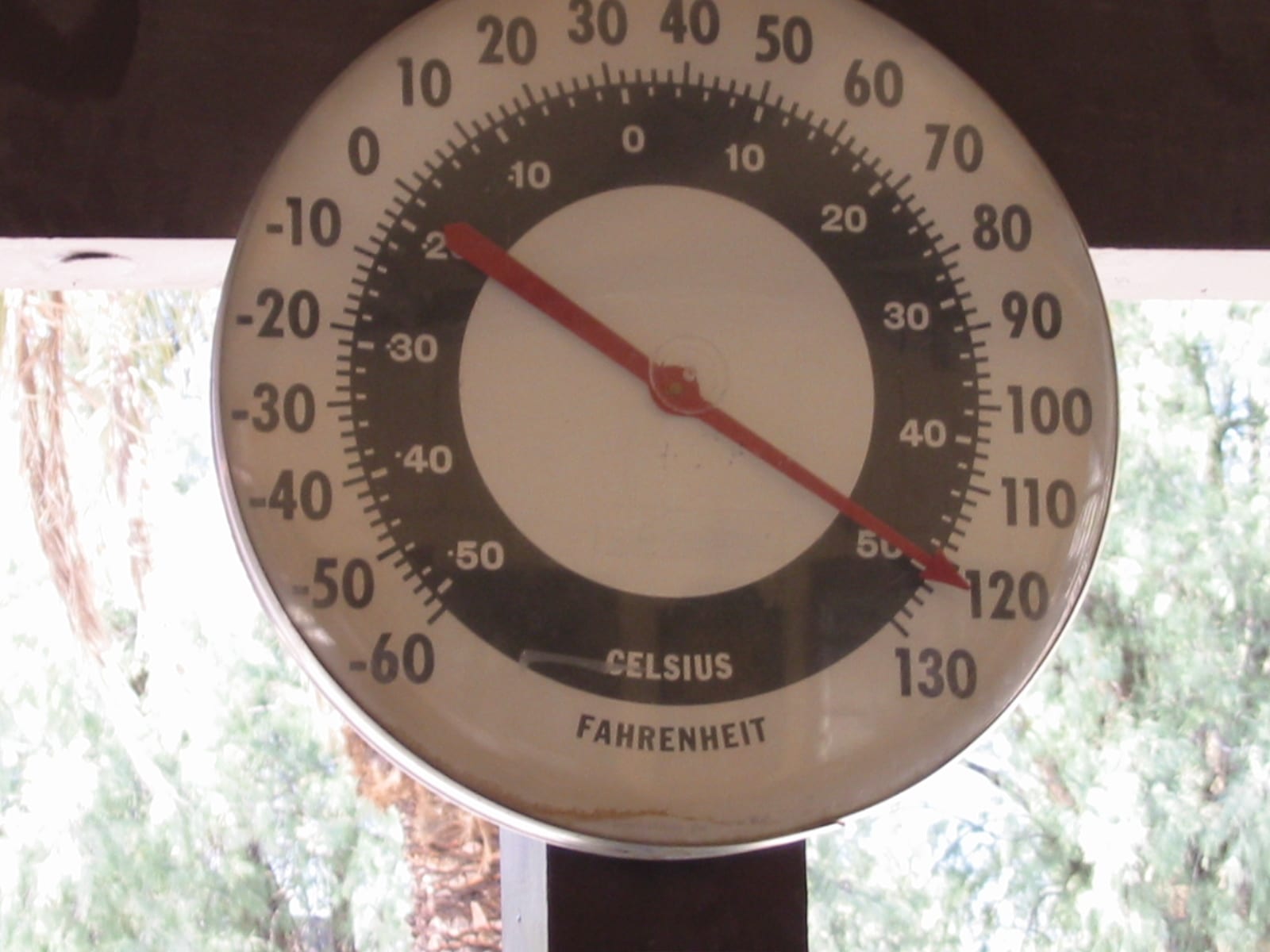 A round dial thermometer with Fahrenheit and Celsius scales, its red needle pointing to about 120 degrees Fahrenheit
