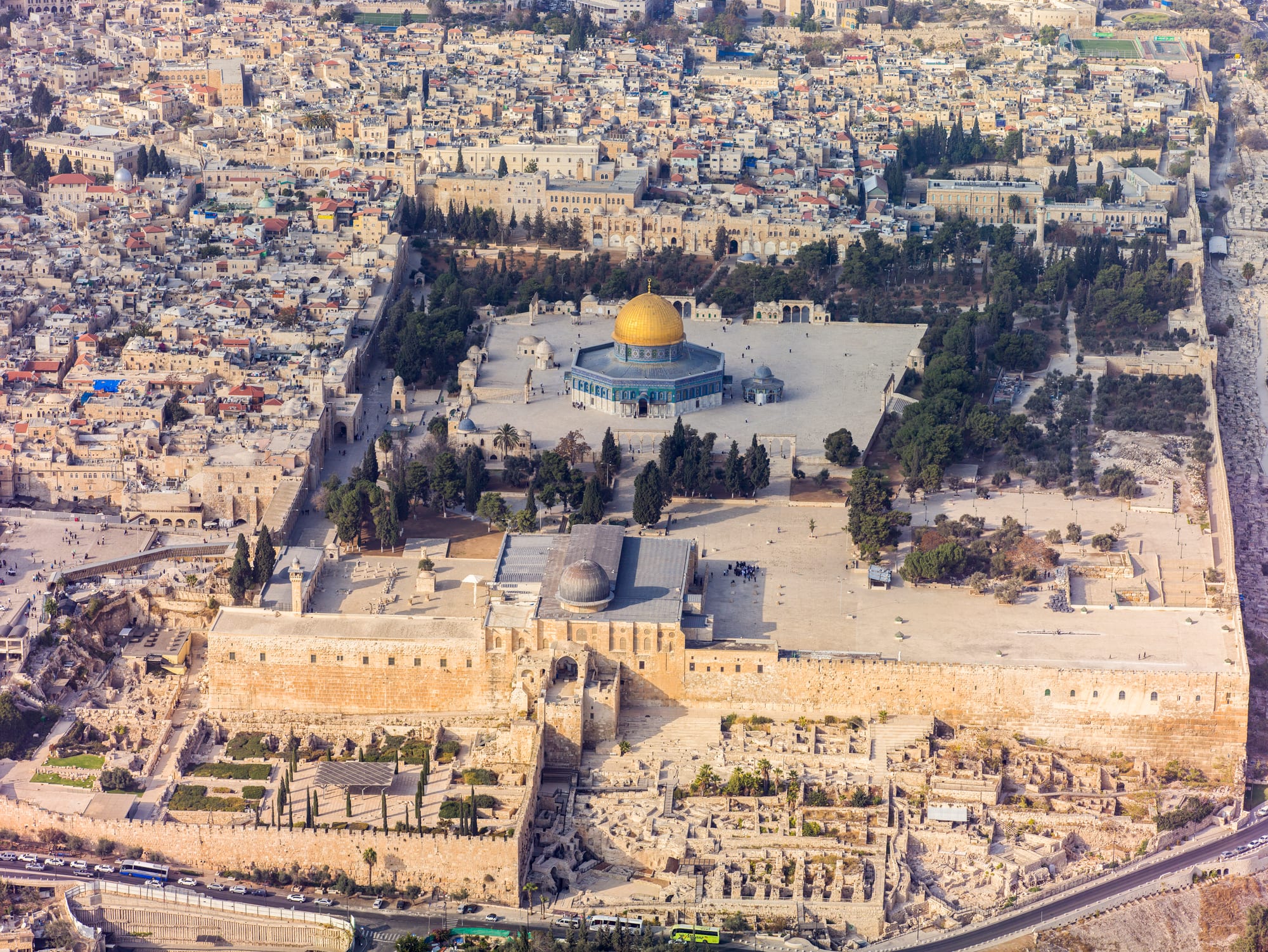 An aerial view of a vast walled stone platform in a dense old city, with a gold-domed octagonal shrine at its centre and a grey-domed mosque at its southern edge
