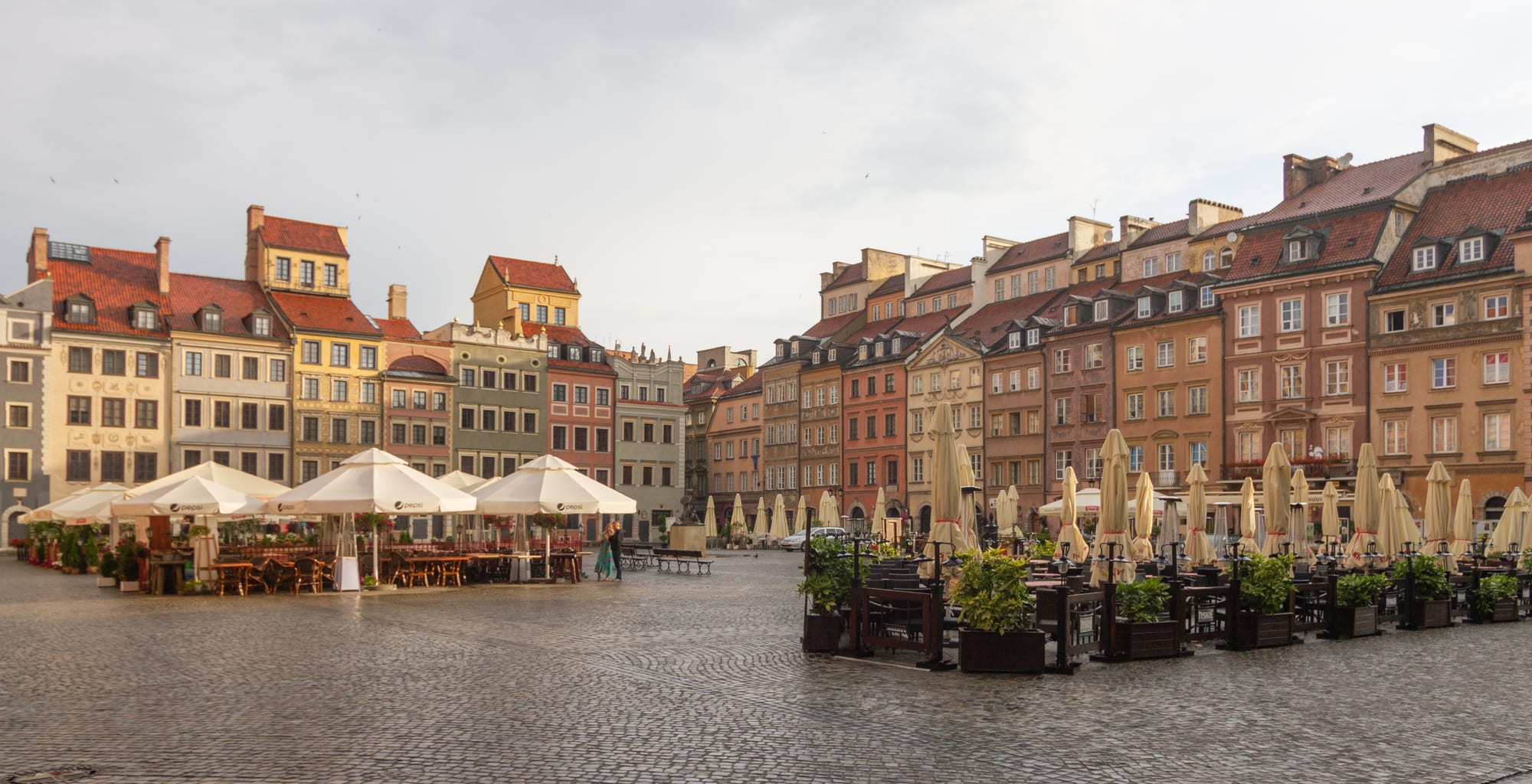 A cobbled square lined with tall, brightly painted townhouses with steep red roofs, and café umbrellas along the pavement