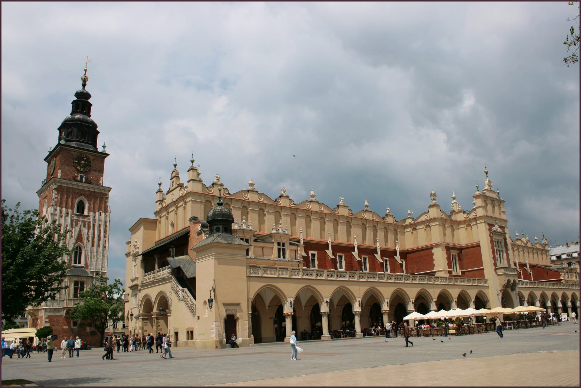 A long Renaissance market hall with arcades and a decorative parapet on a wide paved square, with a tall brick tower to the left