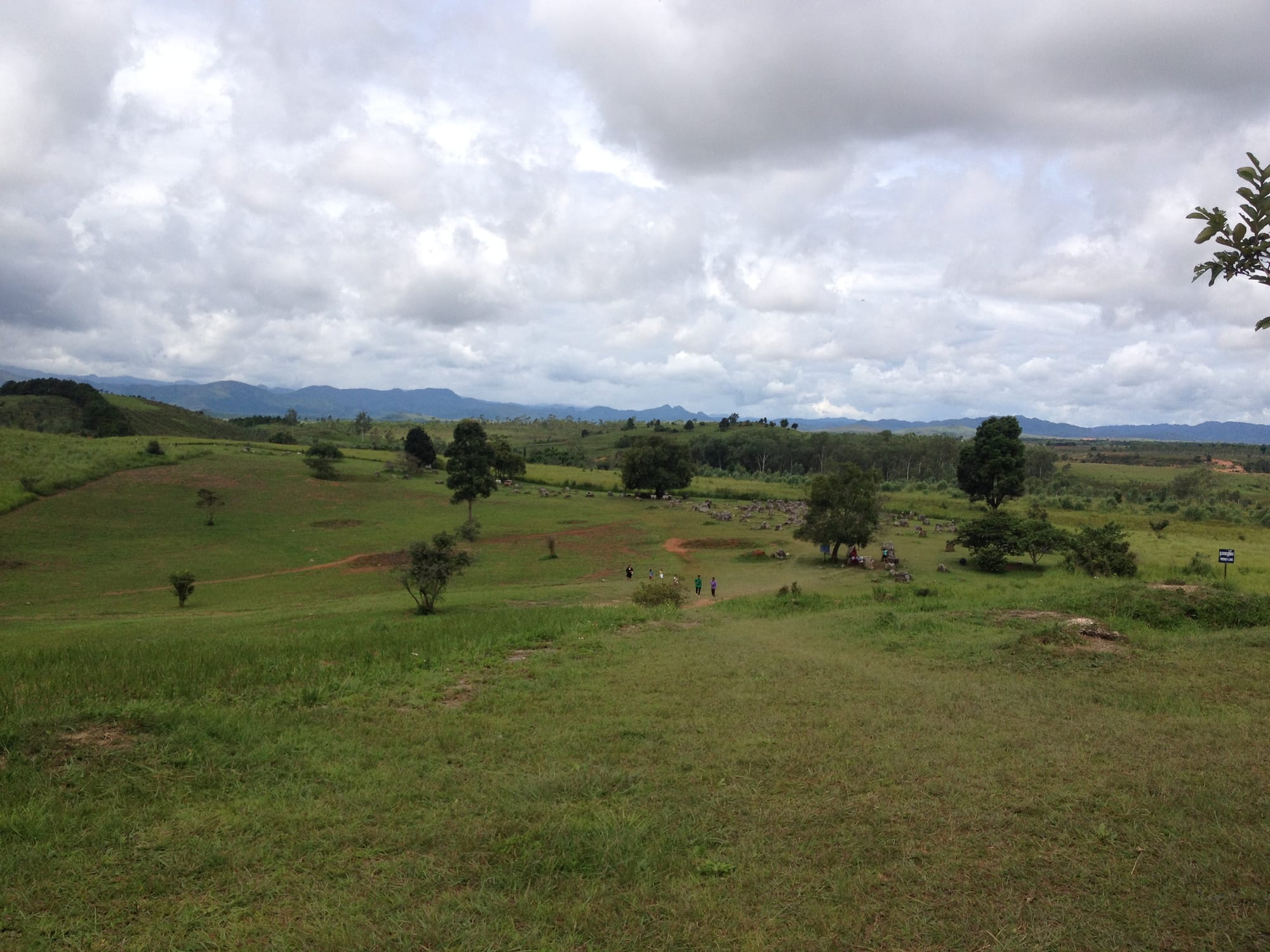Rolling green grassland with groups of grey stone jars and a few visitors in the distance