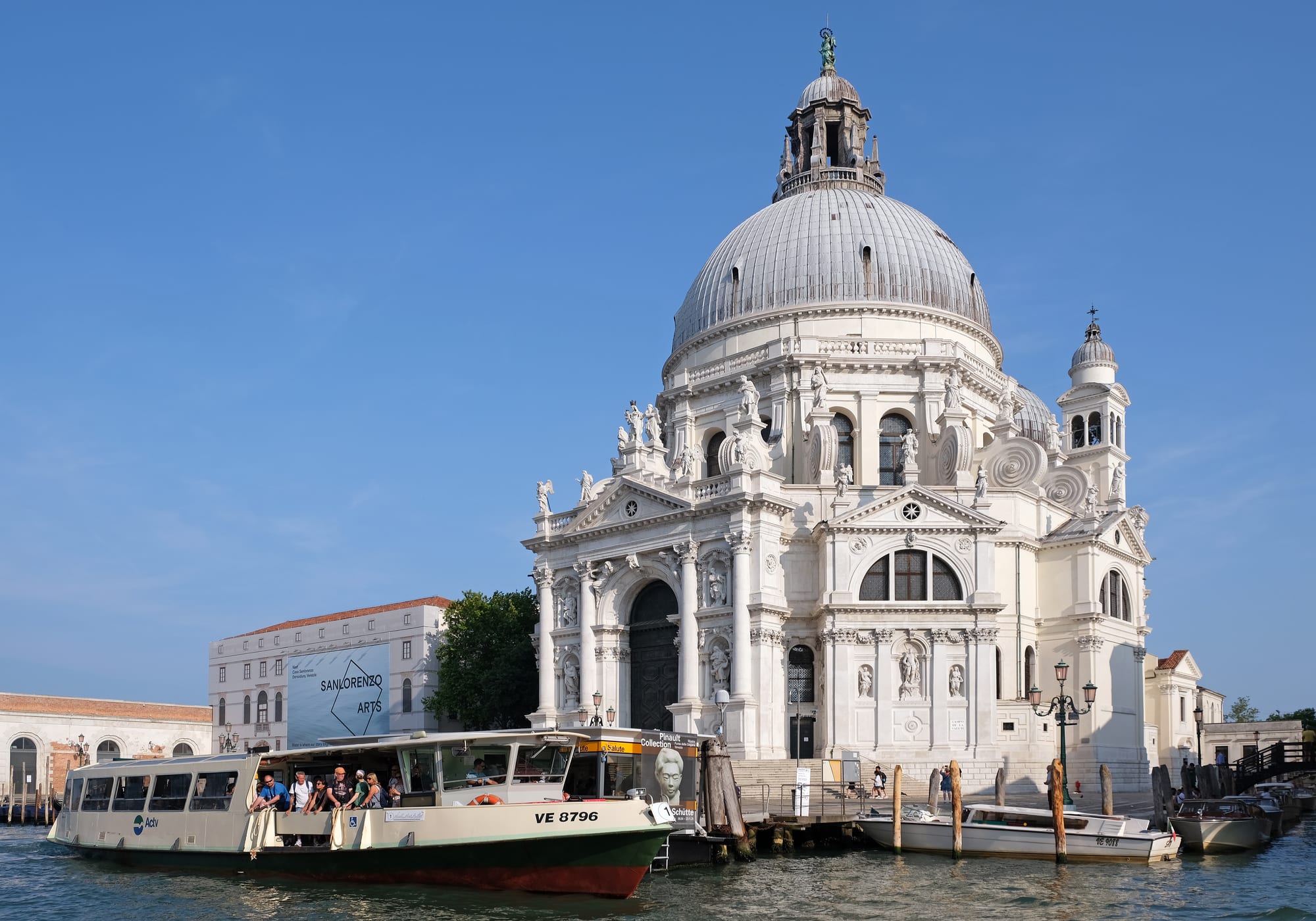 A large white domed baroque church on the edge of a canal, with a water bus pulling up at a stop in front