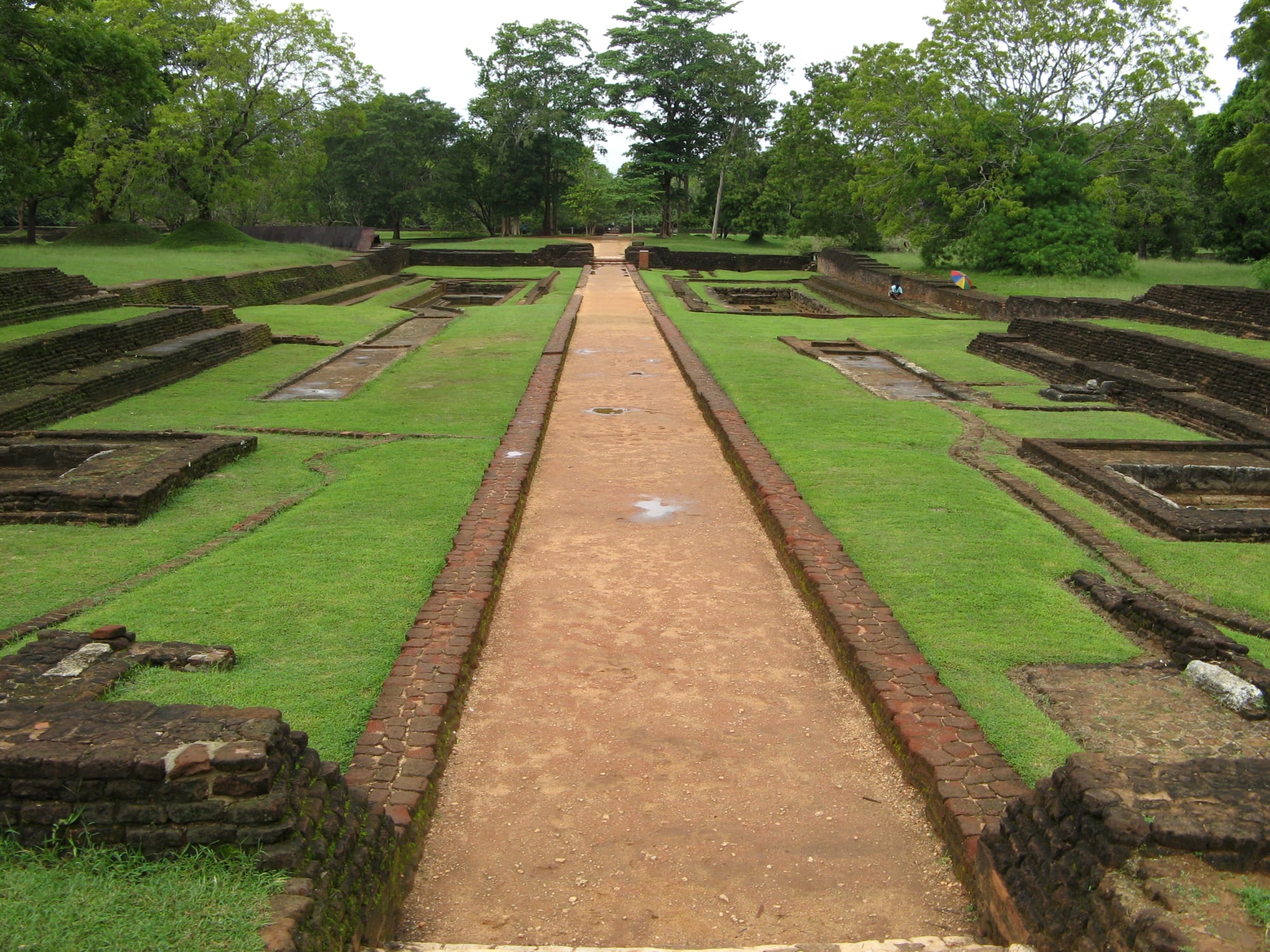 A long straight path between symmetrical brick-edged pools and lawns, leading towards trees