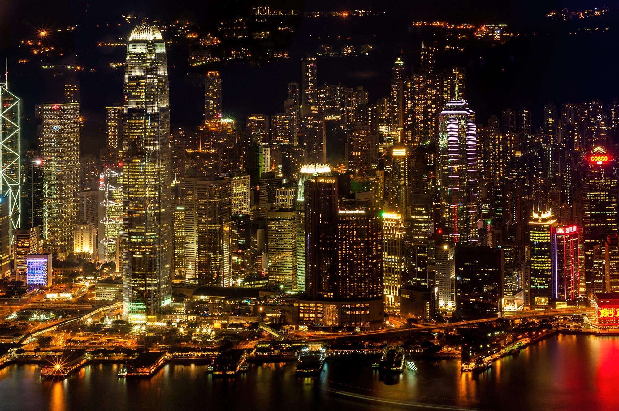 Brightly lit skyscrapers crowded along a harbour front at night