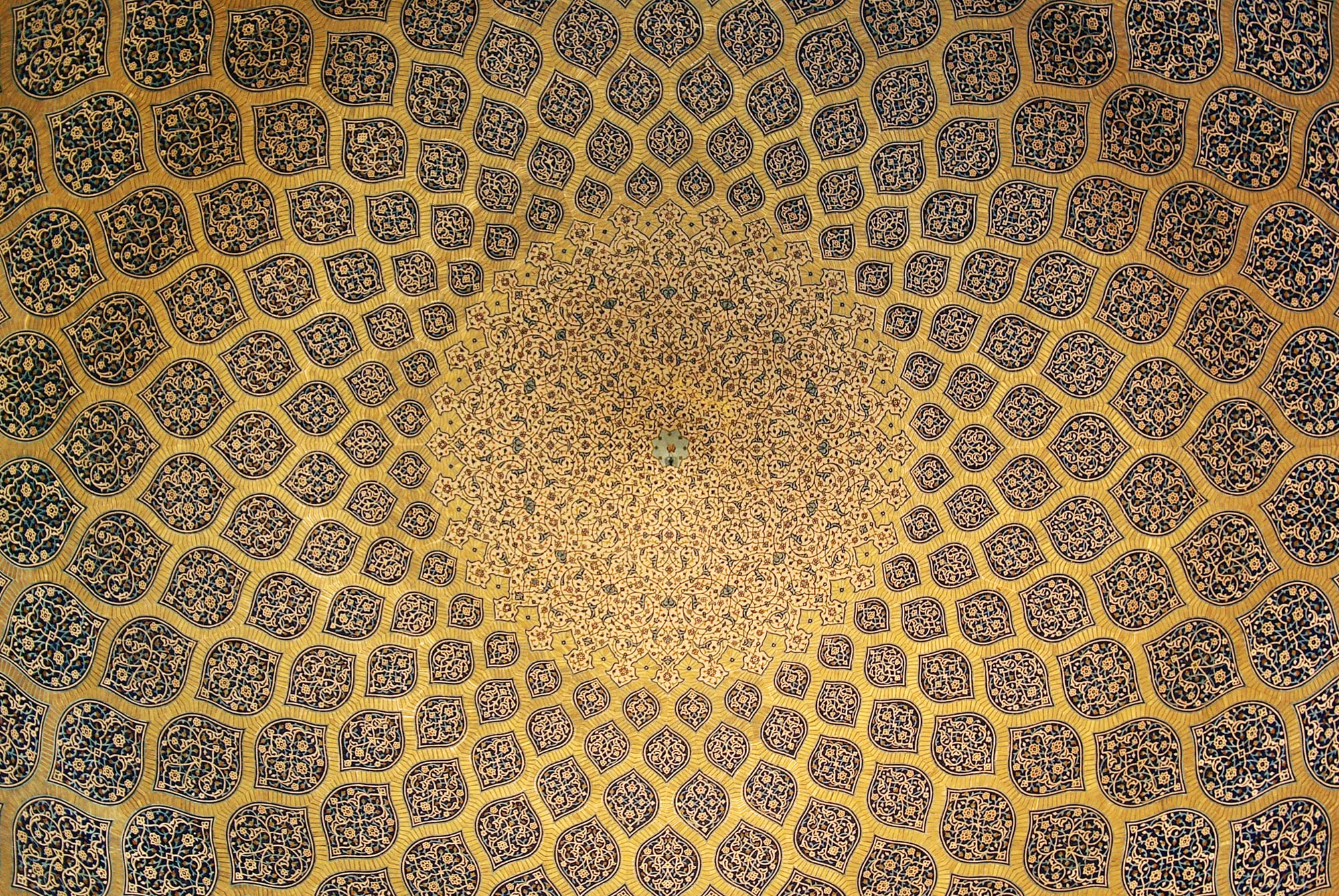 The inside of a dome covered in a golden pattern of lemon-shaped panels that shrink towards the centre