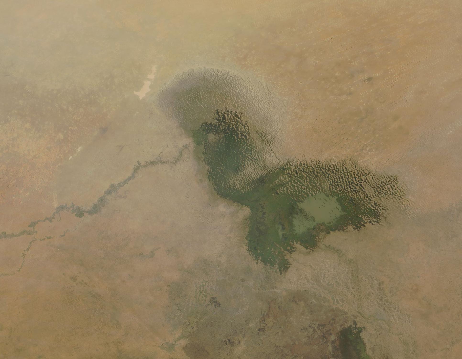 A satellite view of a shrunken green lake with ragged edges surrounded by tan desert and a river winding in from the south-west