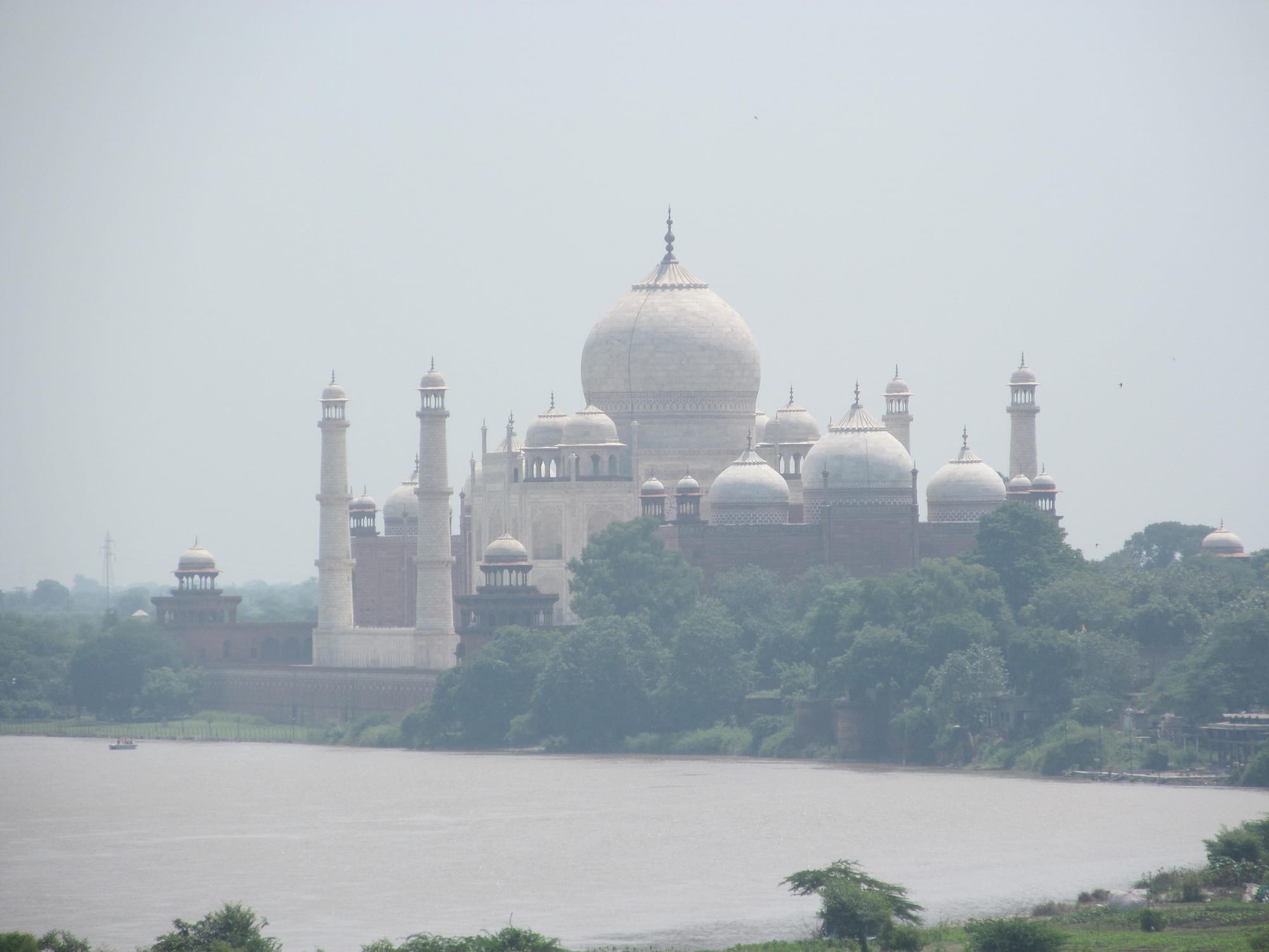 A white marble dome and minarets in hazy light beyond a wide river and trees