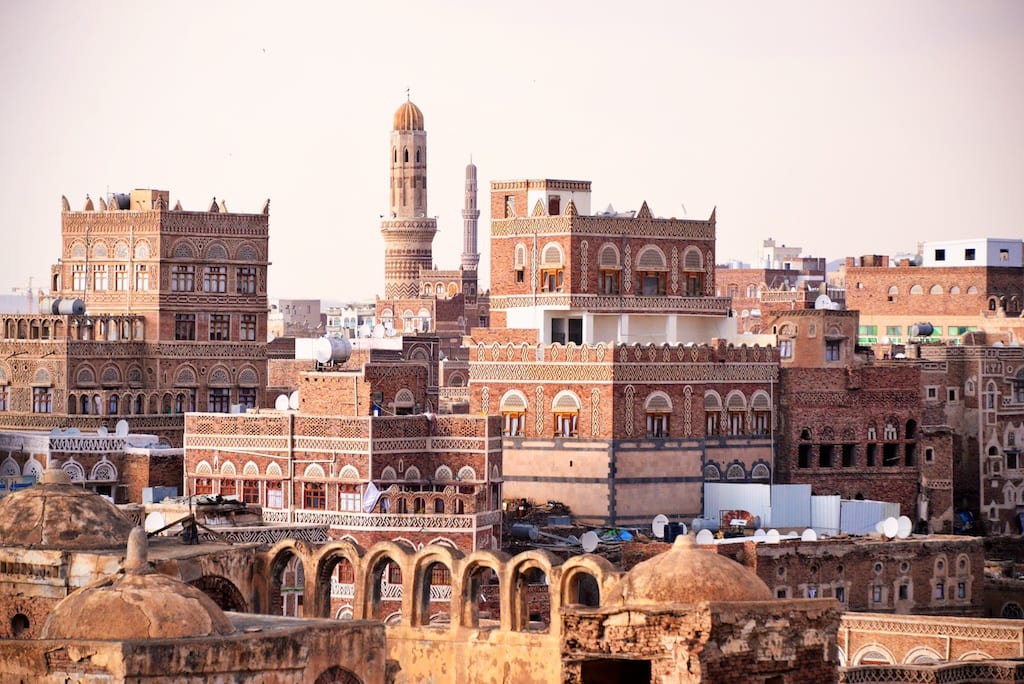 The skyline of Sana'a's Old City, tower-houses decorated with white gypsum tracery rising above older stone ruins