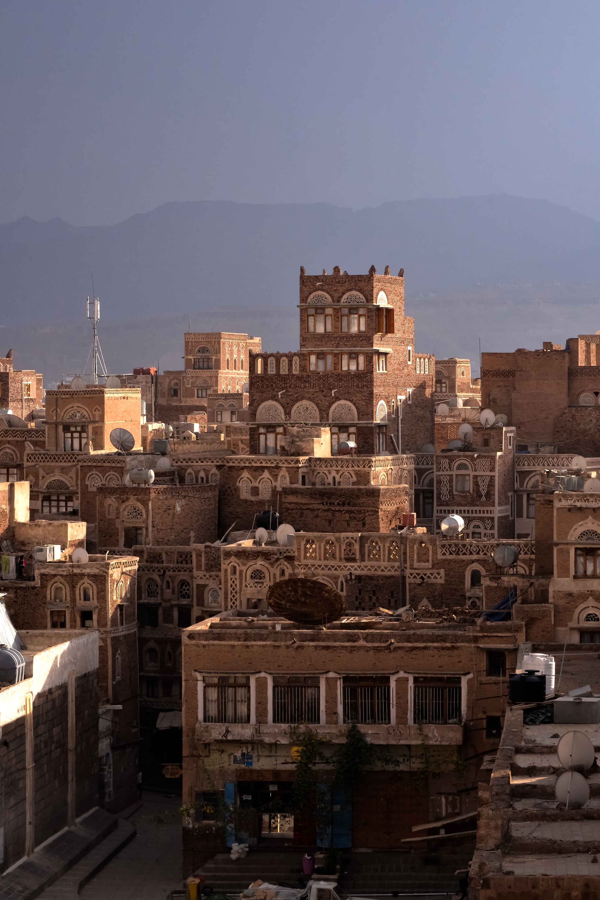 A skyline of tall mud-brick tower houses with white geometric window surrounds packed together in the old city of Sanaa
