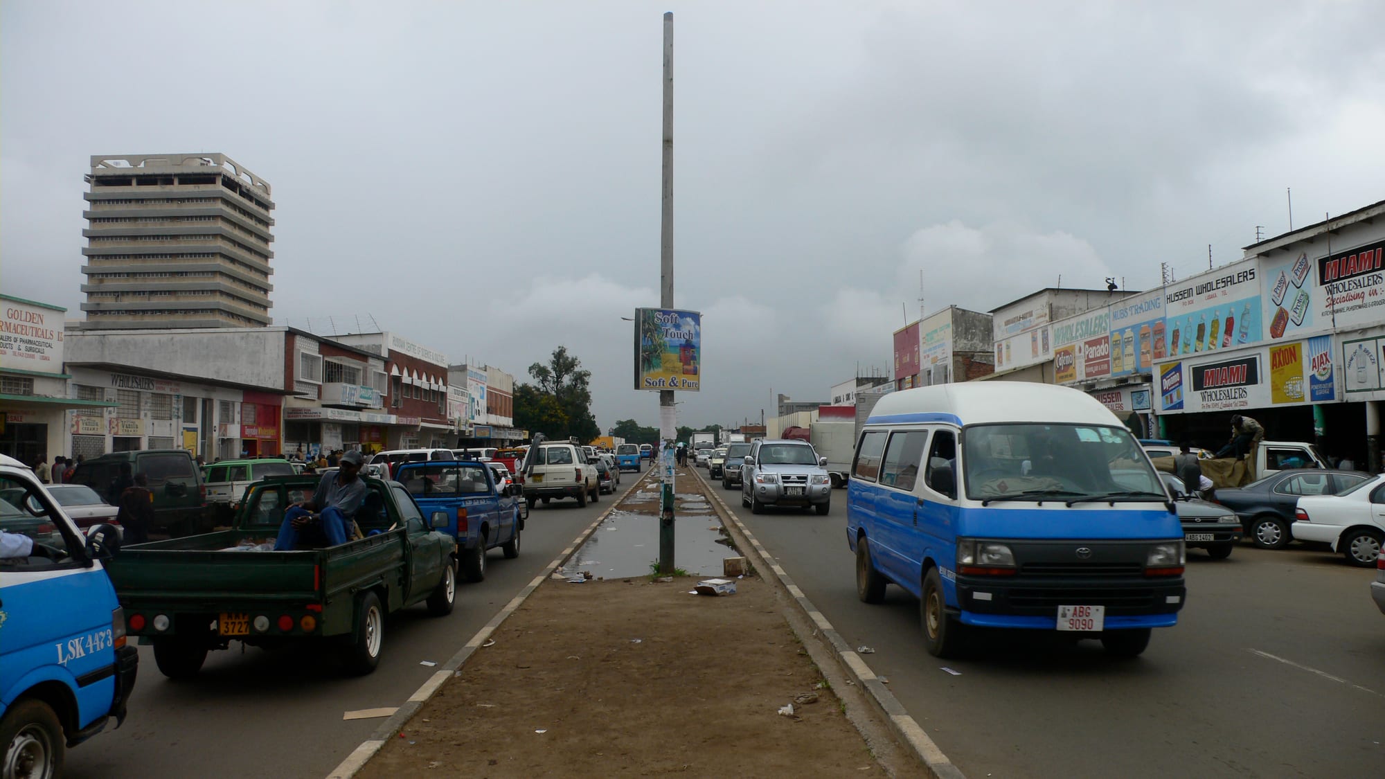 A busy Lusaka street lined with wholesalers' shops, with minibuses and cars queued in traffic