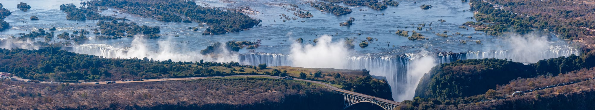 A wide waterfall spanning a river gorge with rising mist
