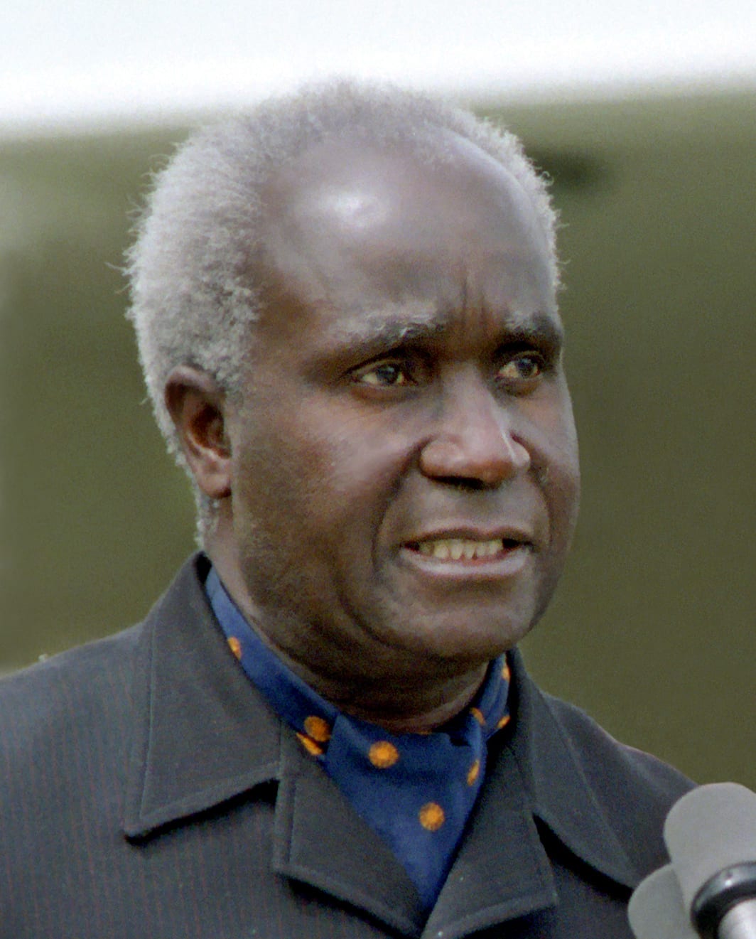 A portrait of Kenneth Kaunda in a dark suit holding a white handkerchief