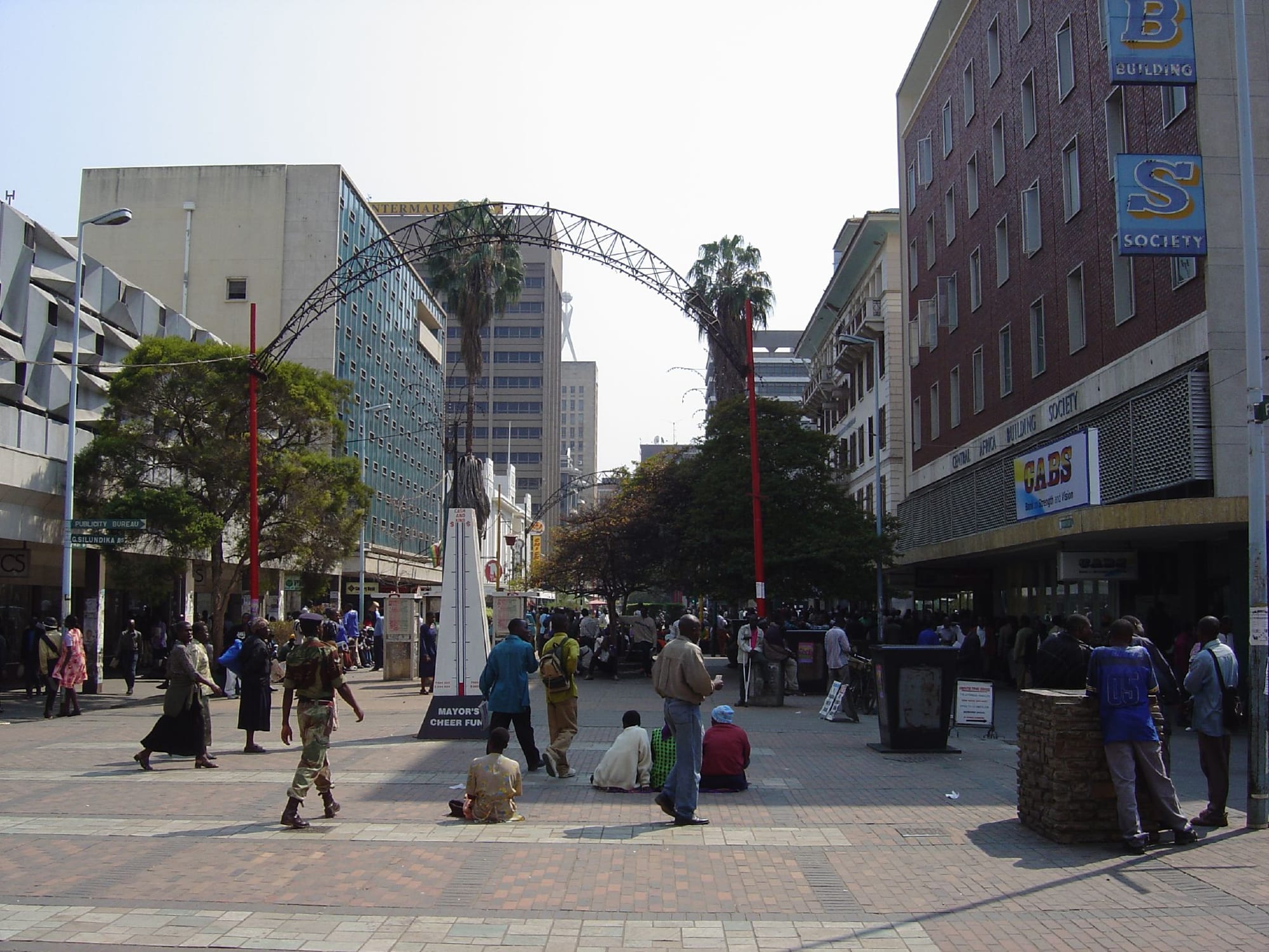 A busy pedestrianised street in central Harare with shoppers and vendors passing under a steel archway over the road