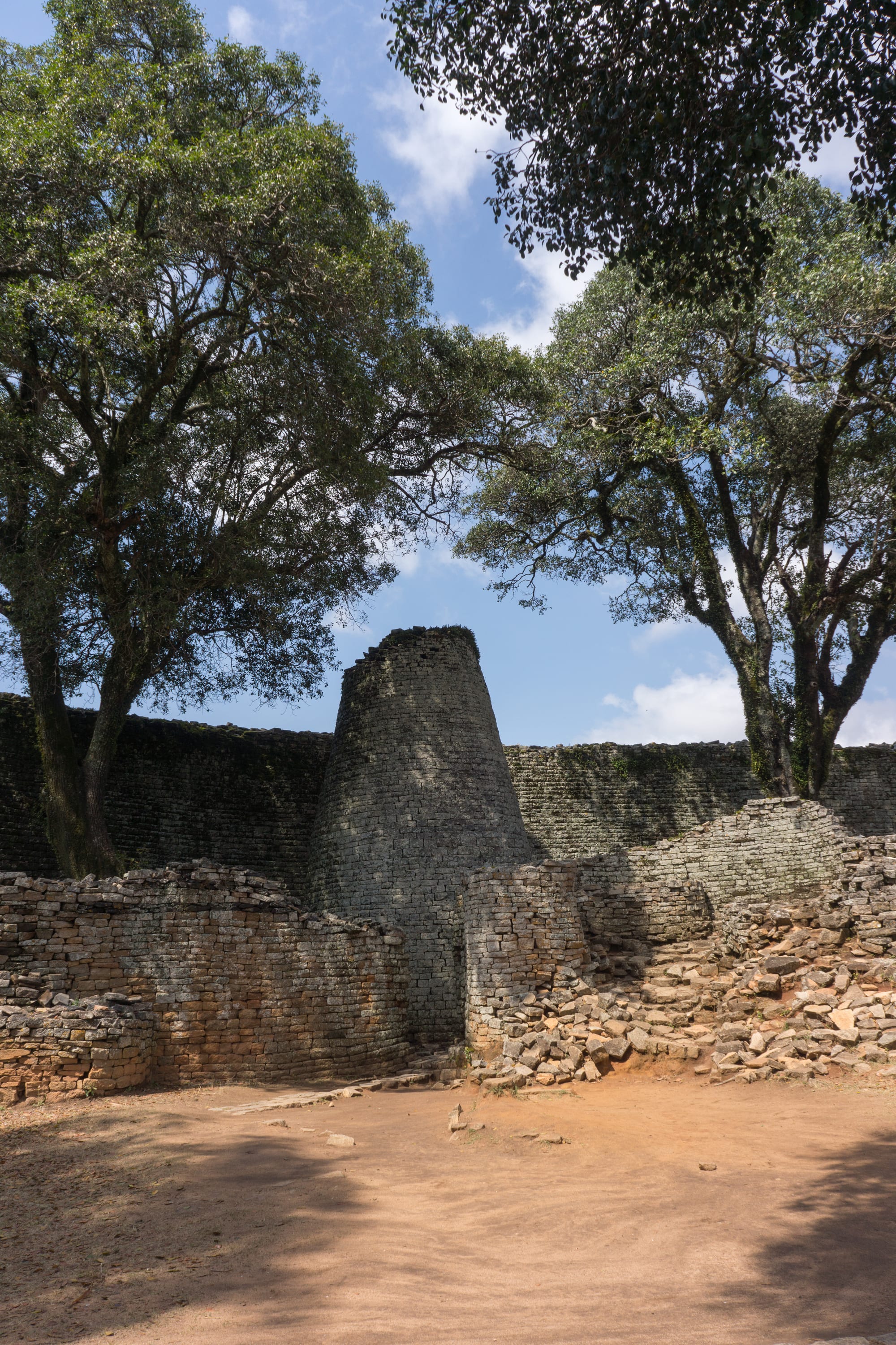 A tall, solid conical tower of fitted stone blocks rising within a curving dry-stone wall at Great Zimbabwe