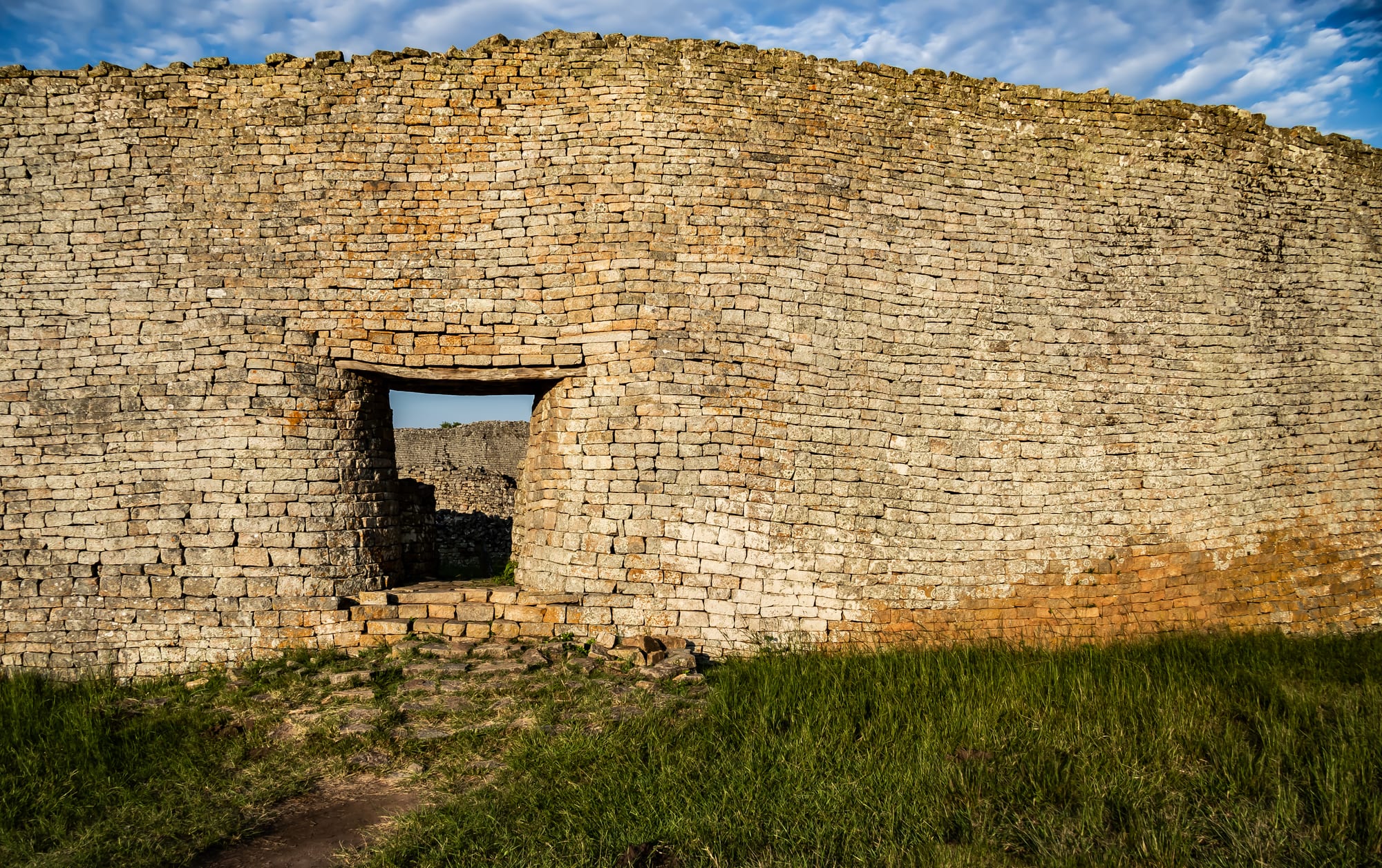 A curving, high dry-stone wall with a stepped entrance at the Great Enclosure of Great Zimbabwe