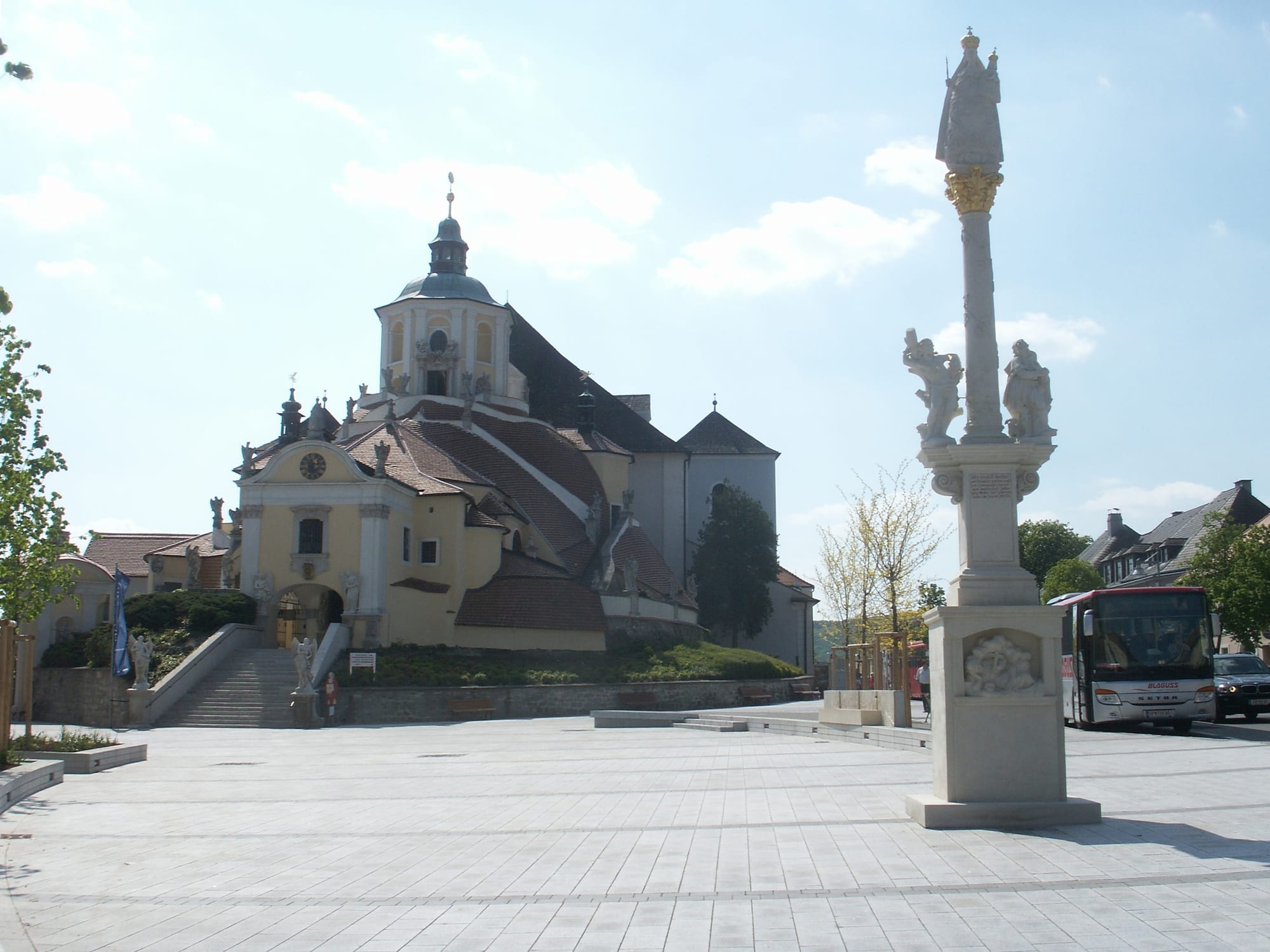 The yellow Baroque Bergkirche with its domed tower and stepped roofs above a paved square with a tall Marian column