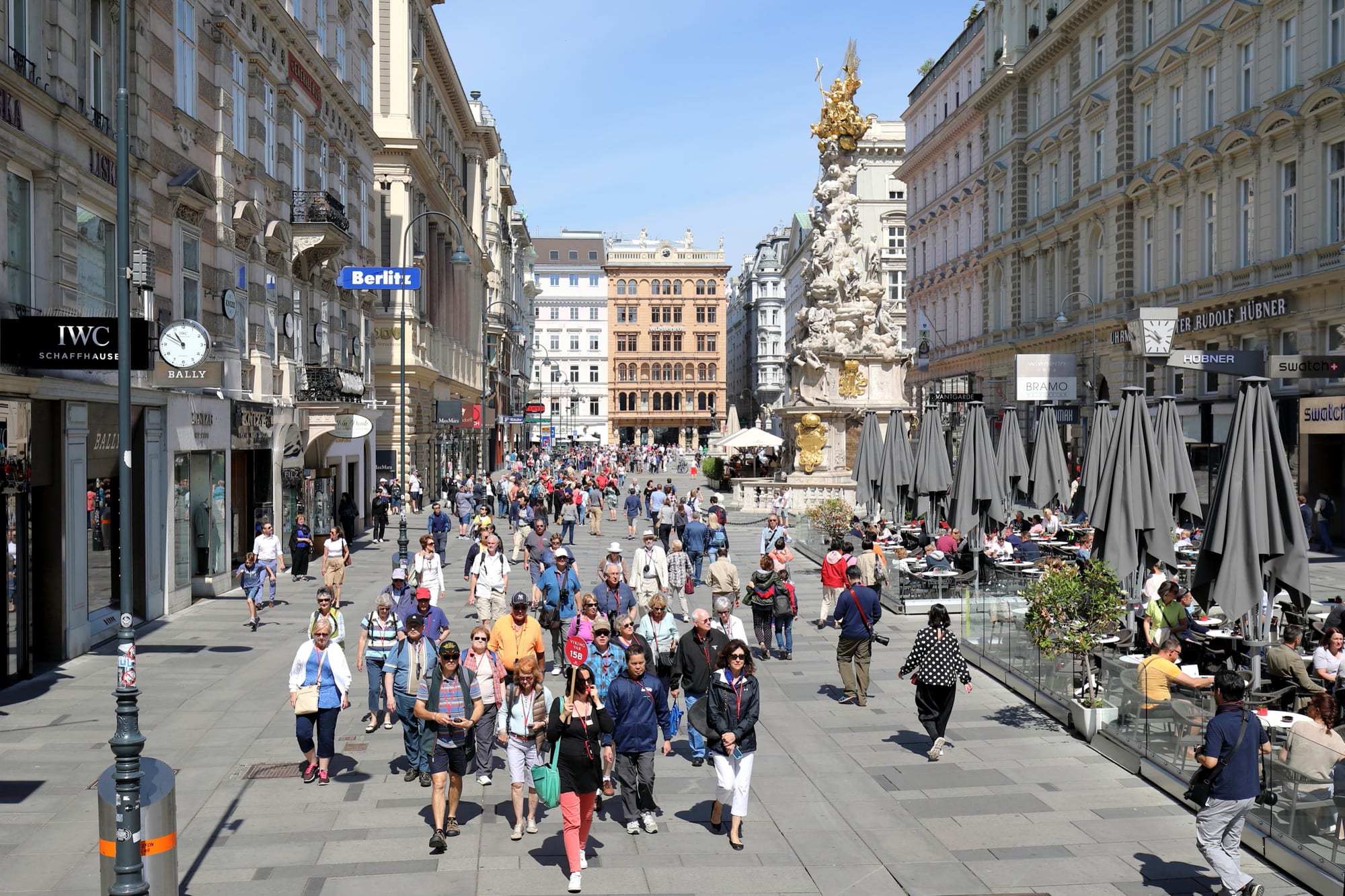 The broad pedestrian Graben lined with grand facades and café umbrellas, with the white and gold Plague Column in the middle