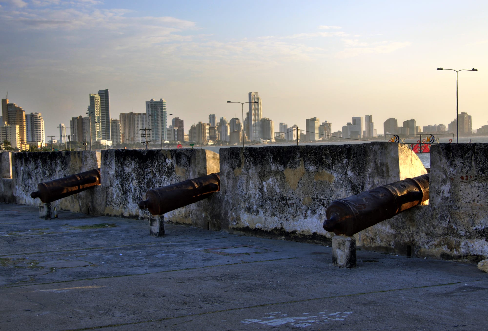 Old iron cannons on the weathered stone walls of Cartagena, with the high-rise towers of Bocagrande across the water
