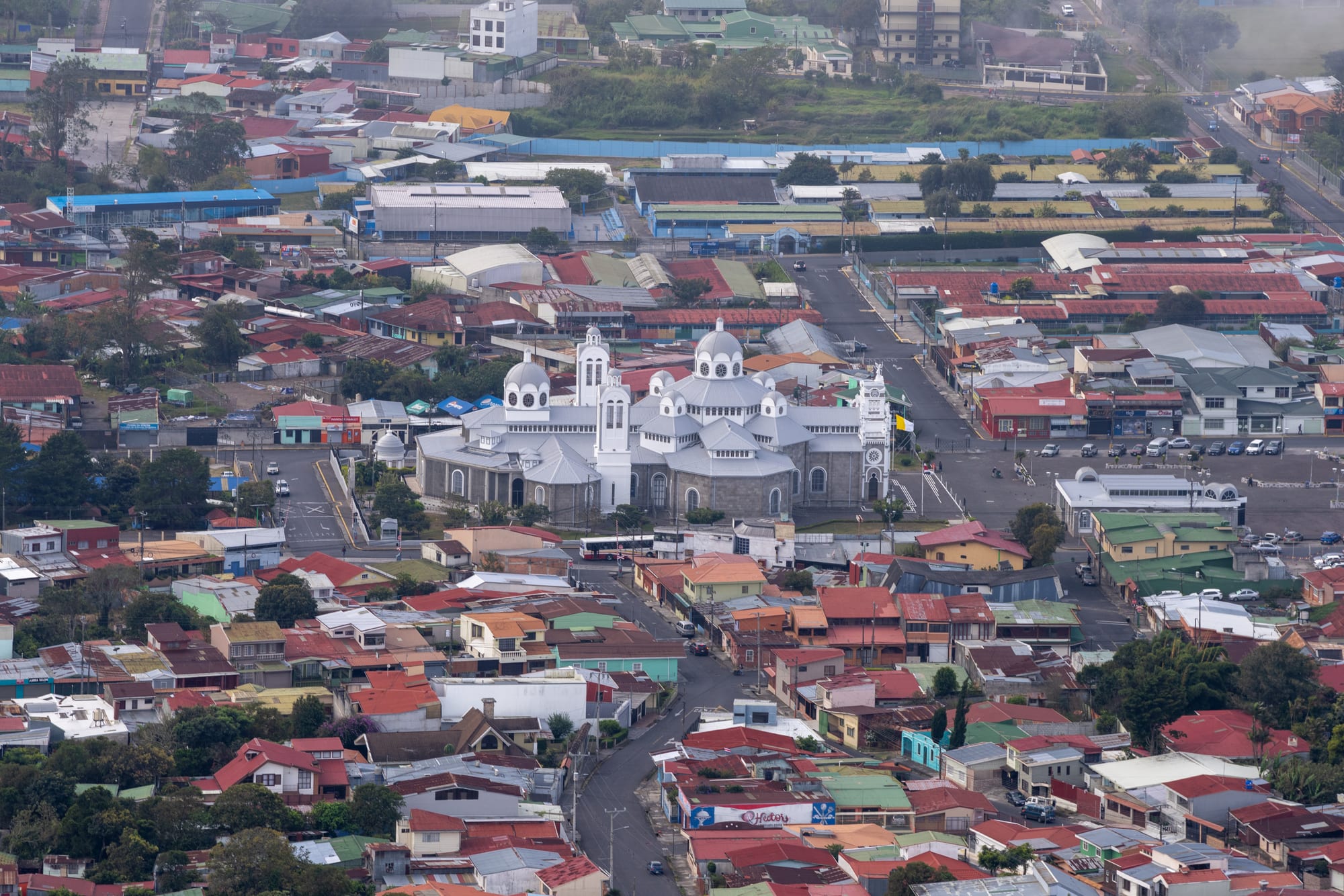Aerial view of a large grey domed basilica with white towers among the red and green roofs of a city