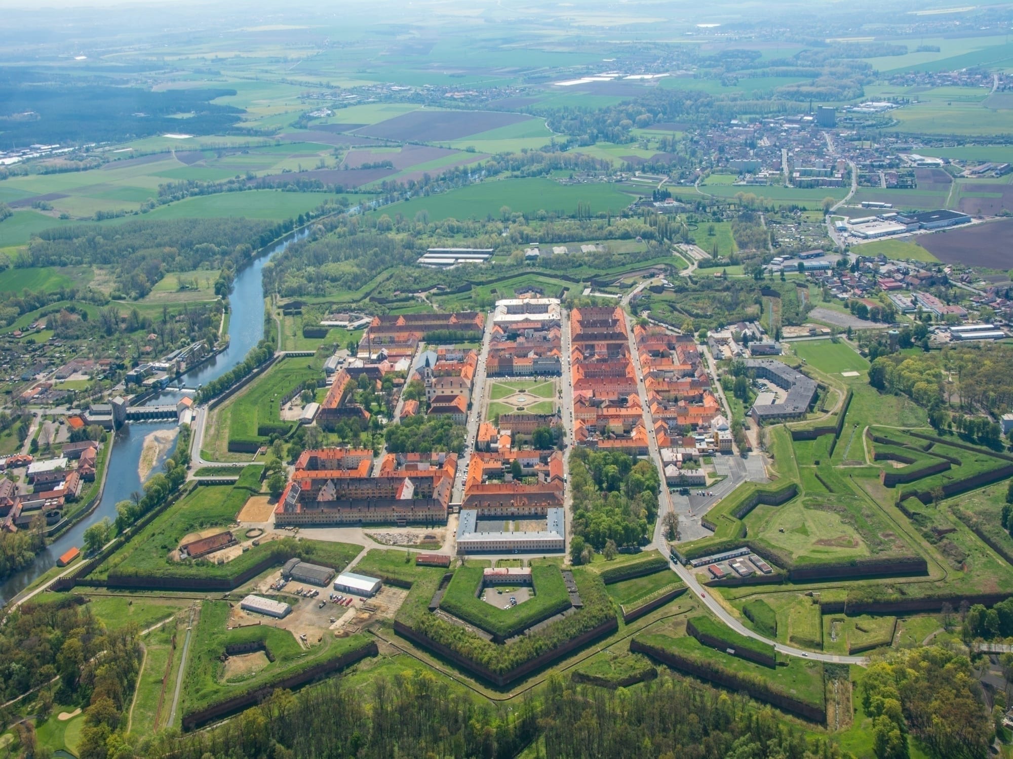 Aerial view of the star-shaped Terezín fortress, with a grid of red-roofed barracks inside grassy ramparts beside a river