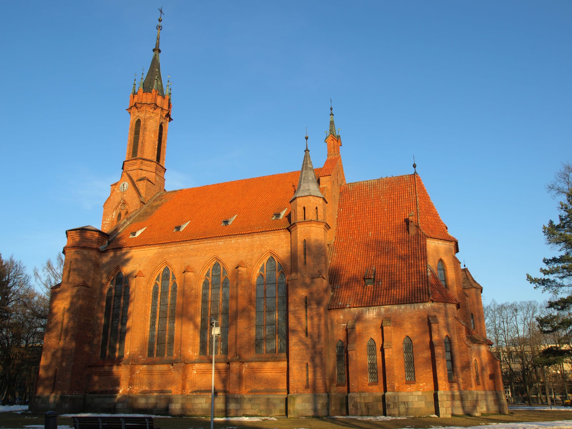A tall red-brick church with a pointed spire and steep orange roof under a clear blue sky