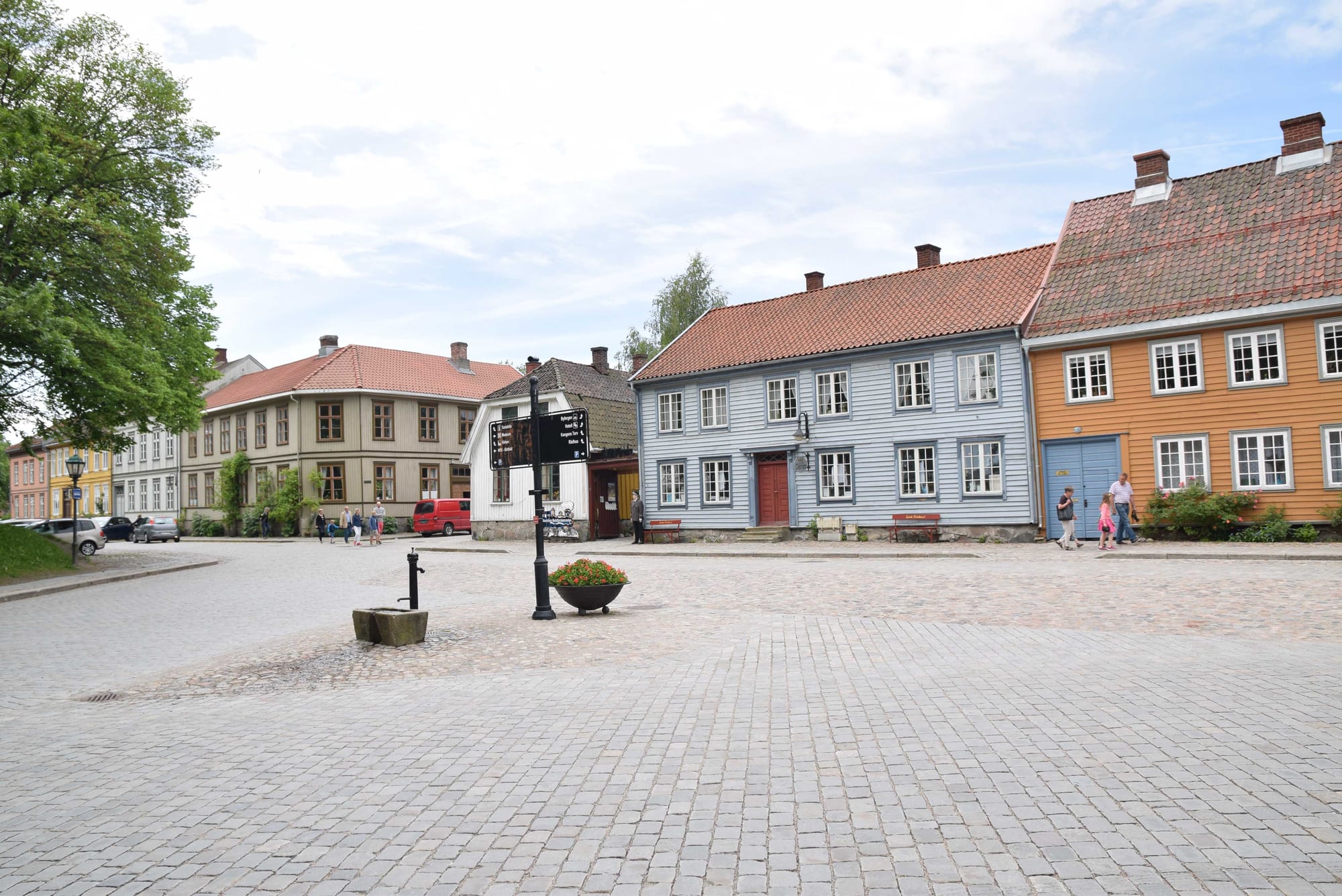 Cobbled square lined with painted wooden houses in blue, orange and cream under red tile roofs, with a few people walking